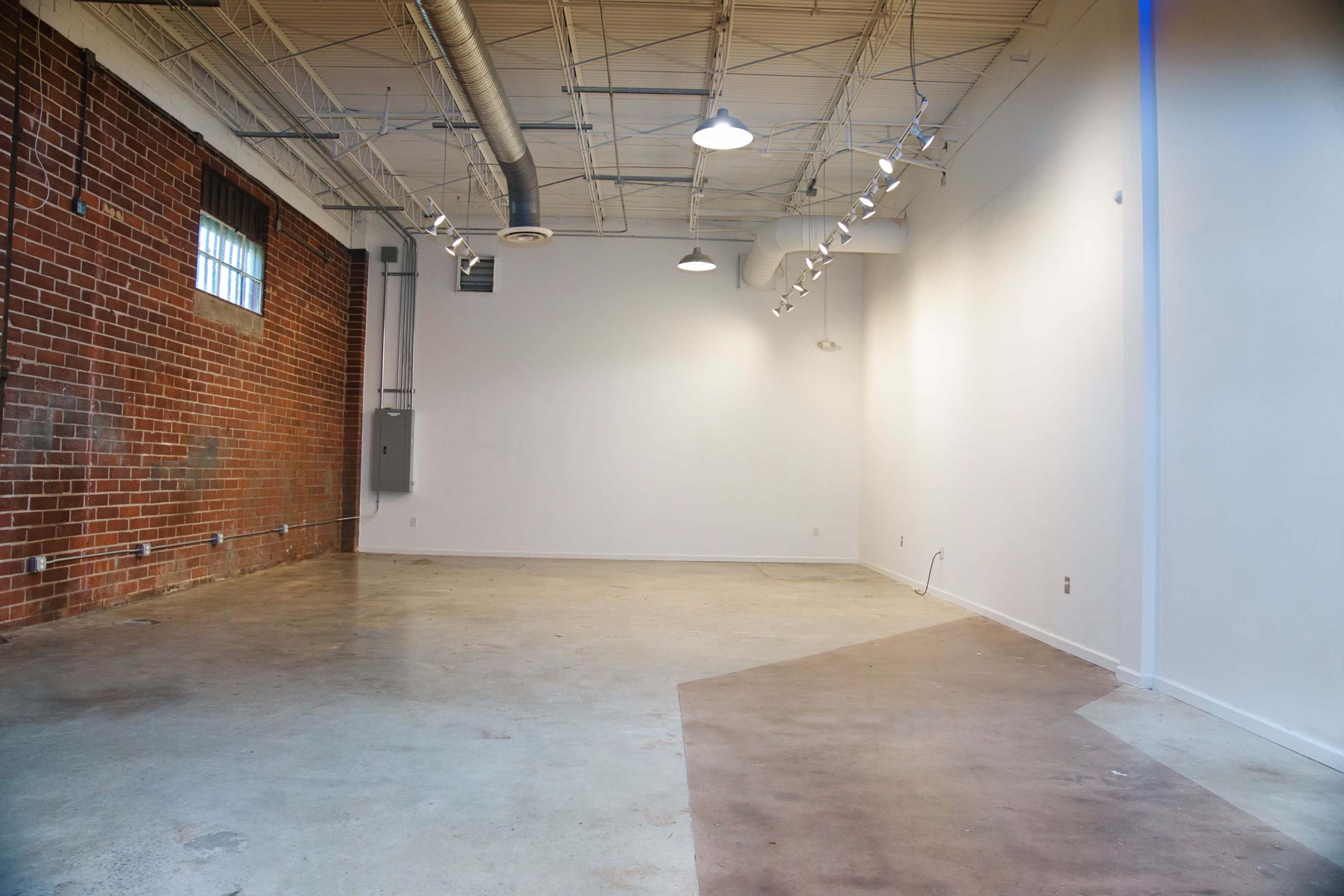 A spacious, empty indoor area with exposed brick walls on one side and a plain white wall on the other.