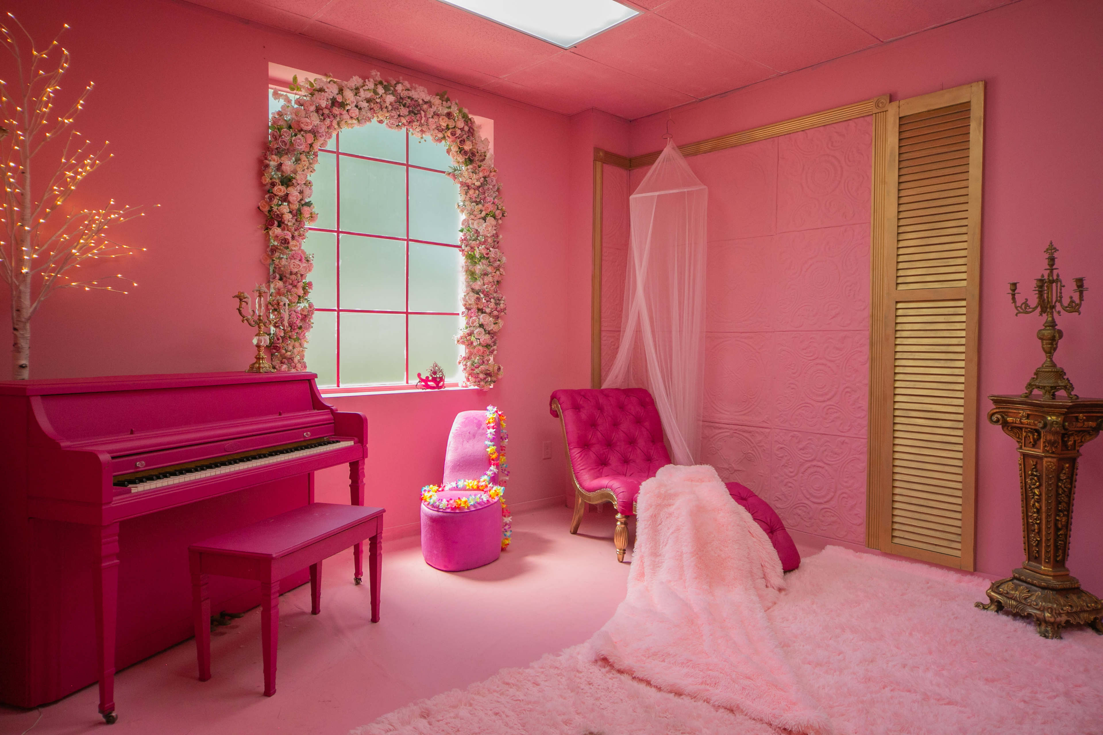 The room features pink walls, a pink piano, a velvet chair, and floral decorations around a window.