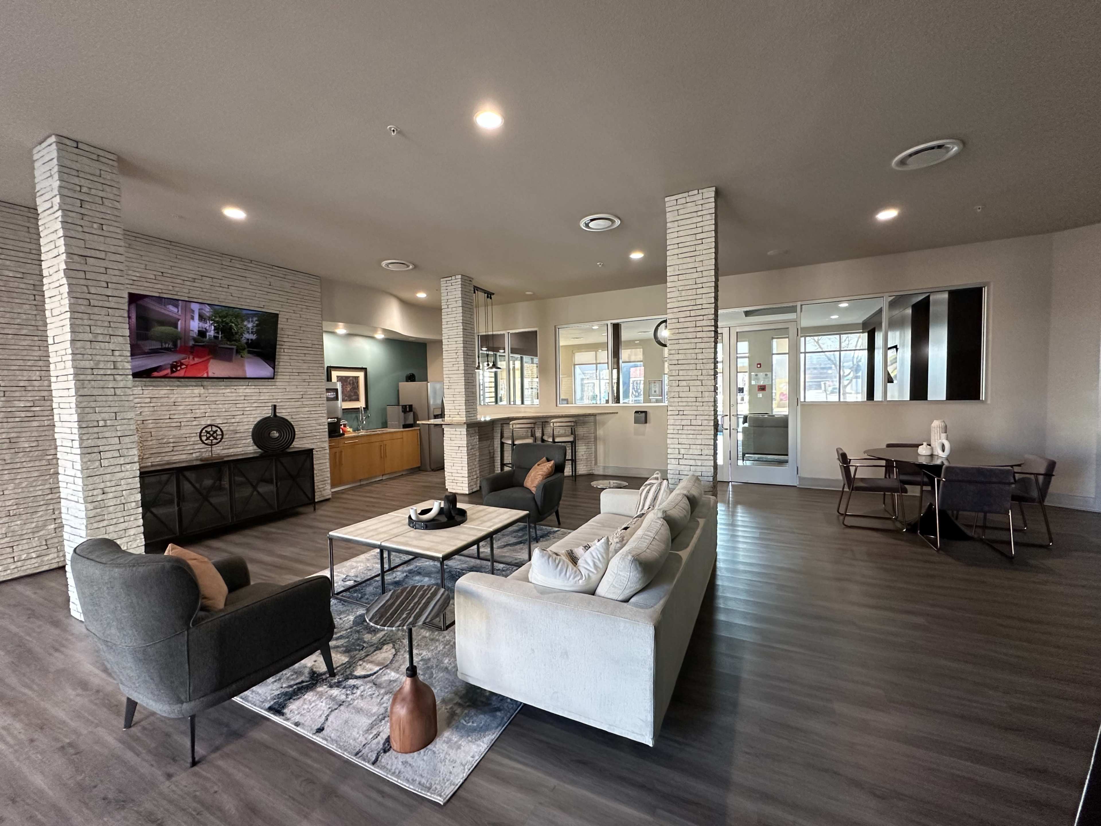 The image shows a modern lobby area with seating, a coffee table, and large windows, featuring a television mounted on the wall.