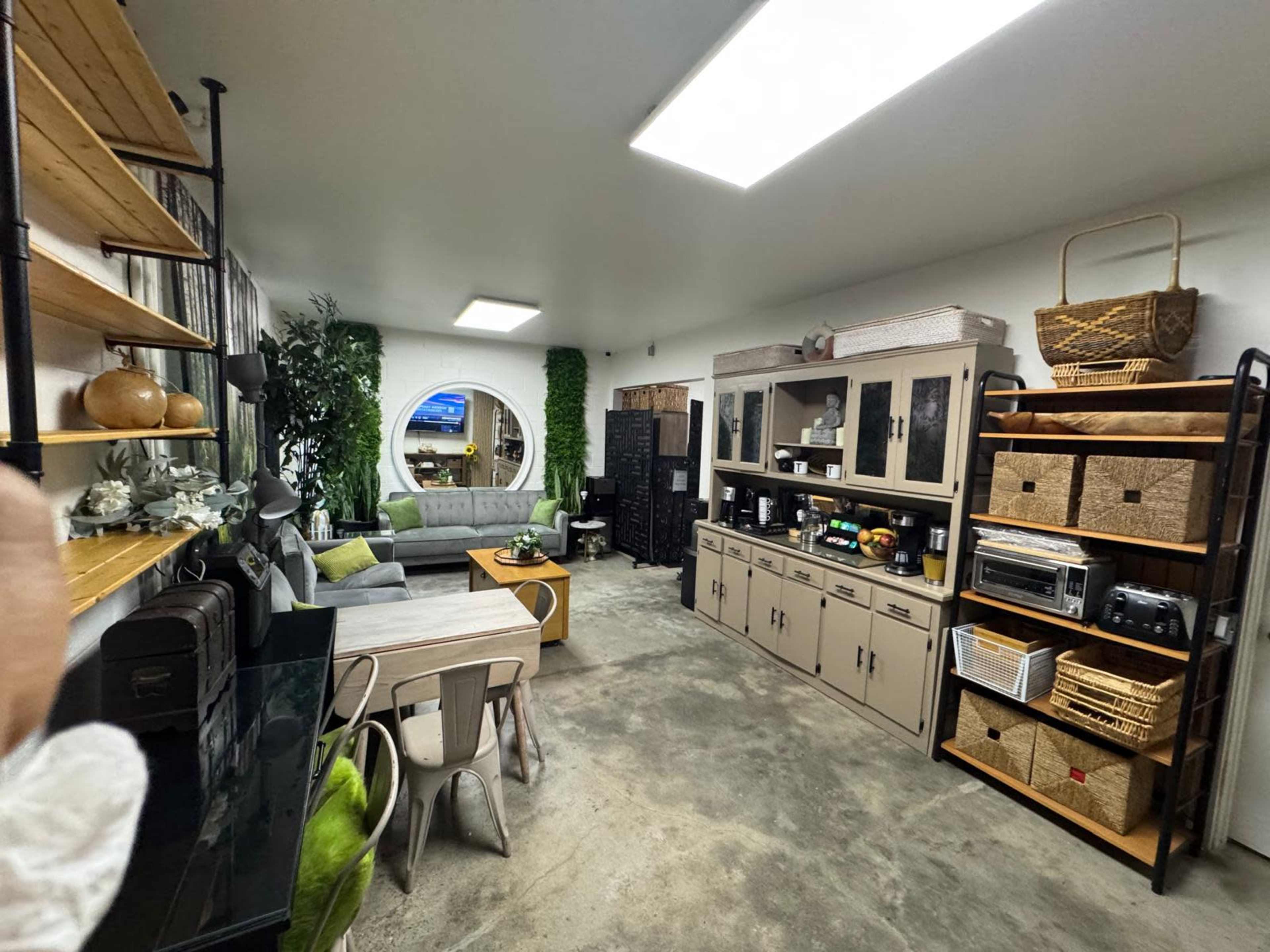 The image shows a modern living space with a gray sectional sofa, a wooden coffee table, and a gallery-style wall of shelves filled with decorative items and small appliances.