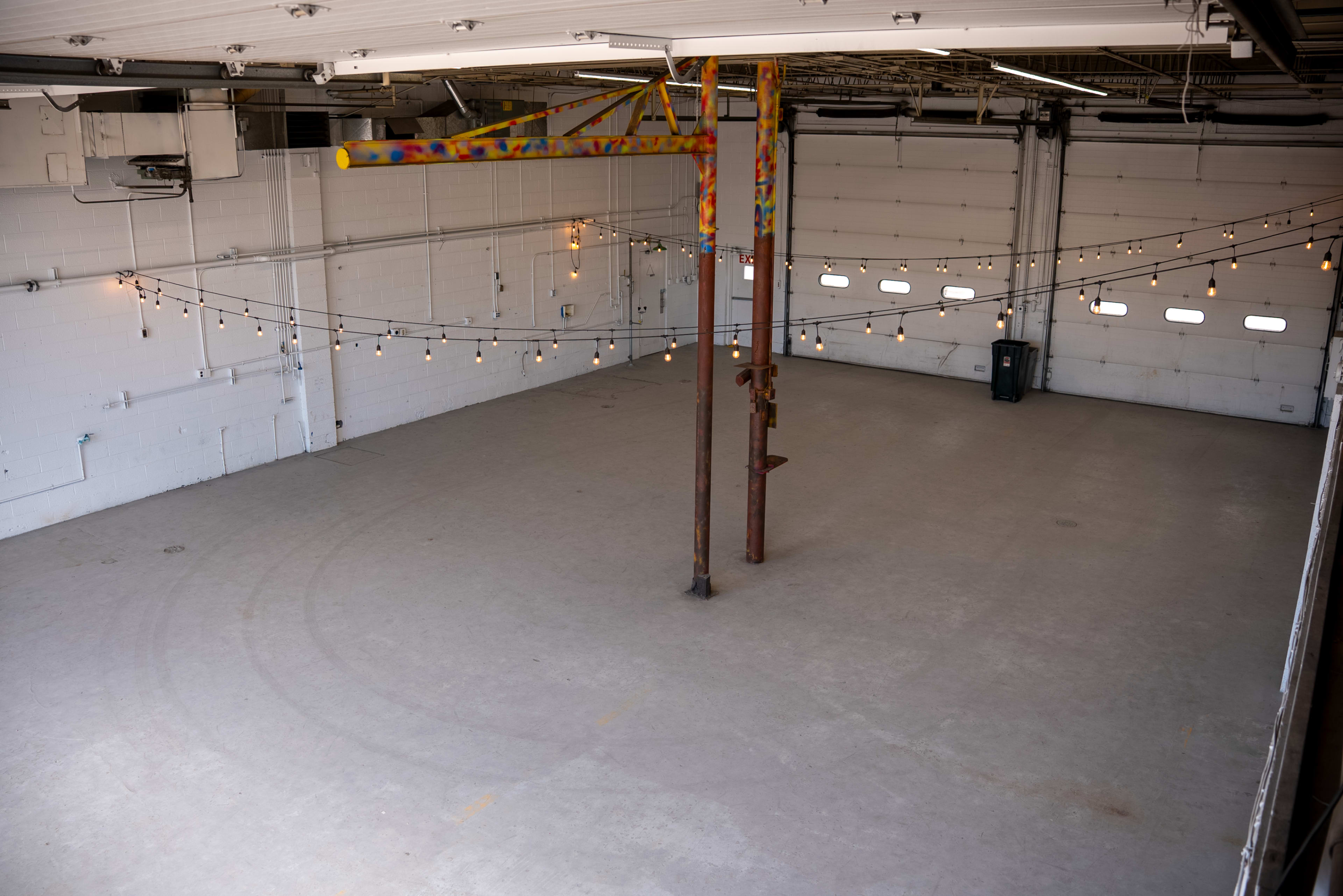 The image shows an empty industrial space with overhead lights strung across the ceiling beams.