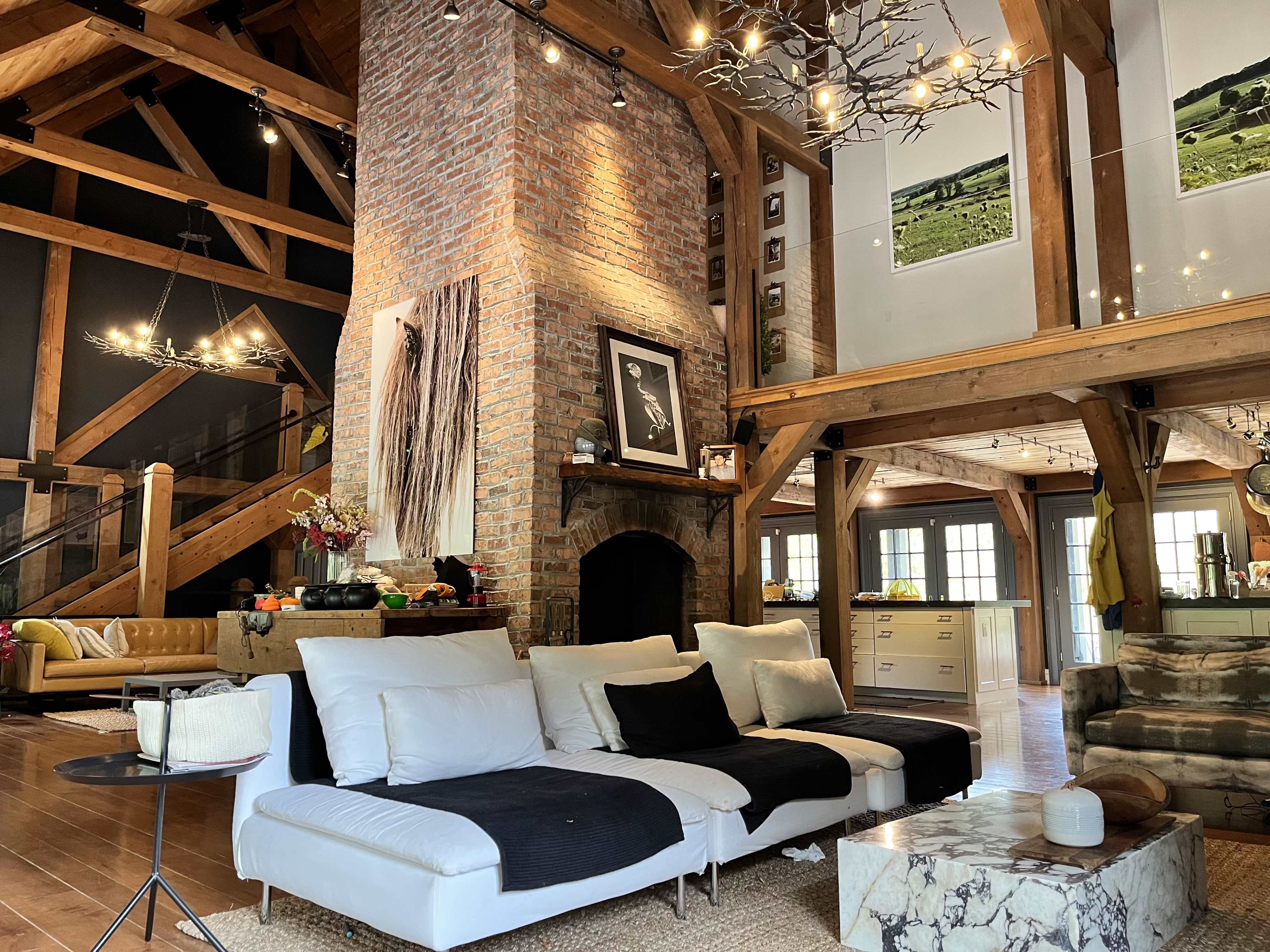 A spacious living area with exposed wooden beams, a brick fireplace, and a mix of contemporary and rustic furniture.