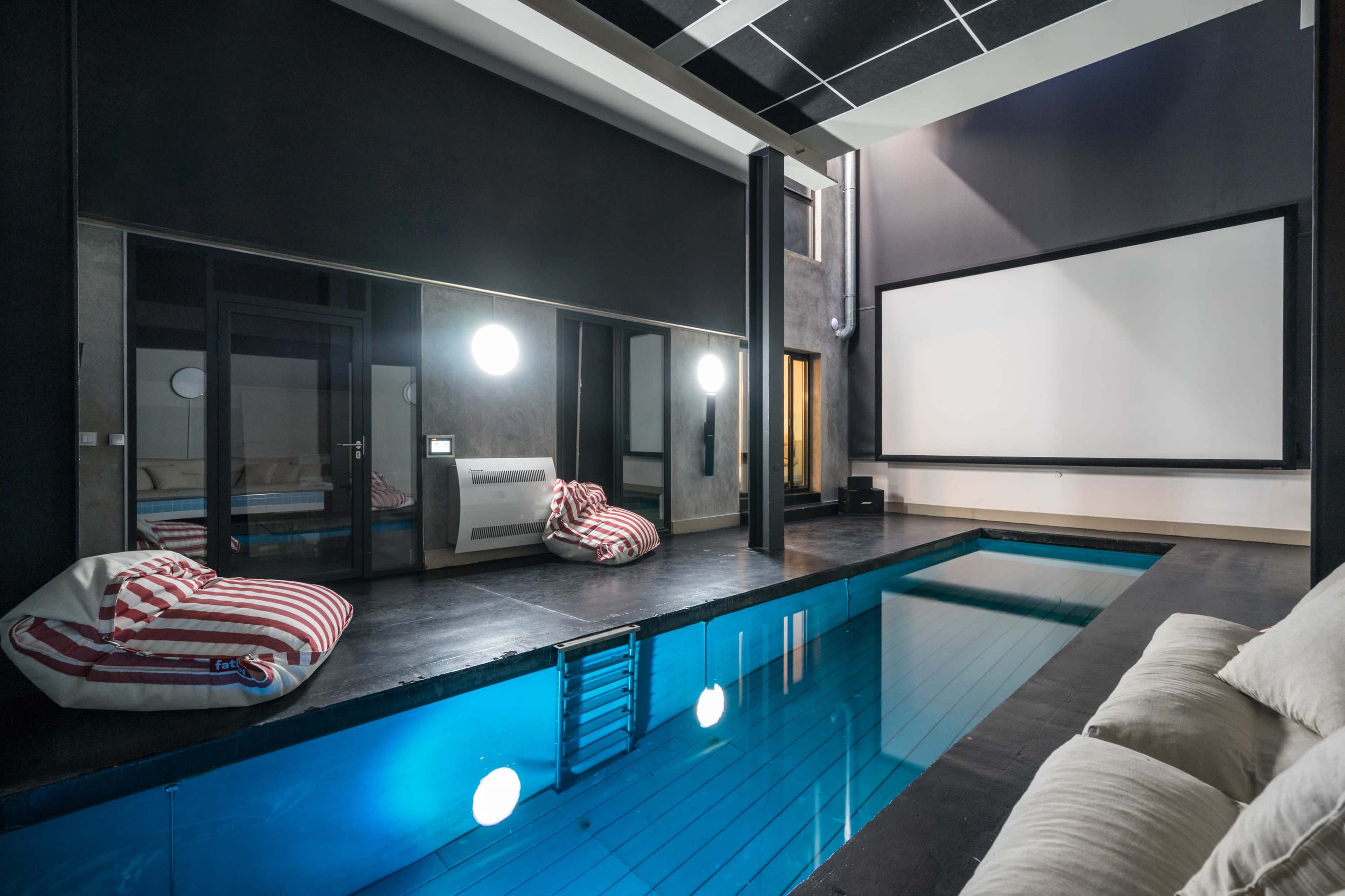An indoor pool area with a large movie screen, bean bag chairs, and a mirrored wall reflecting the pool.