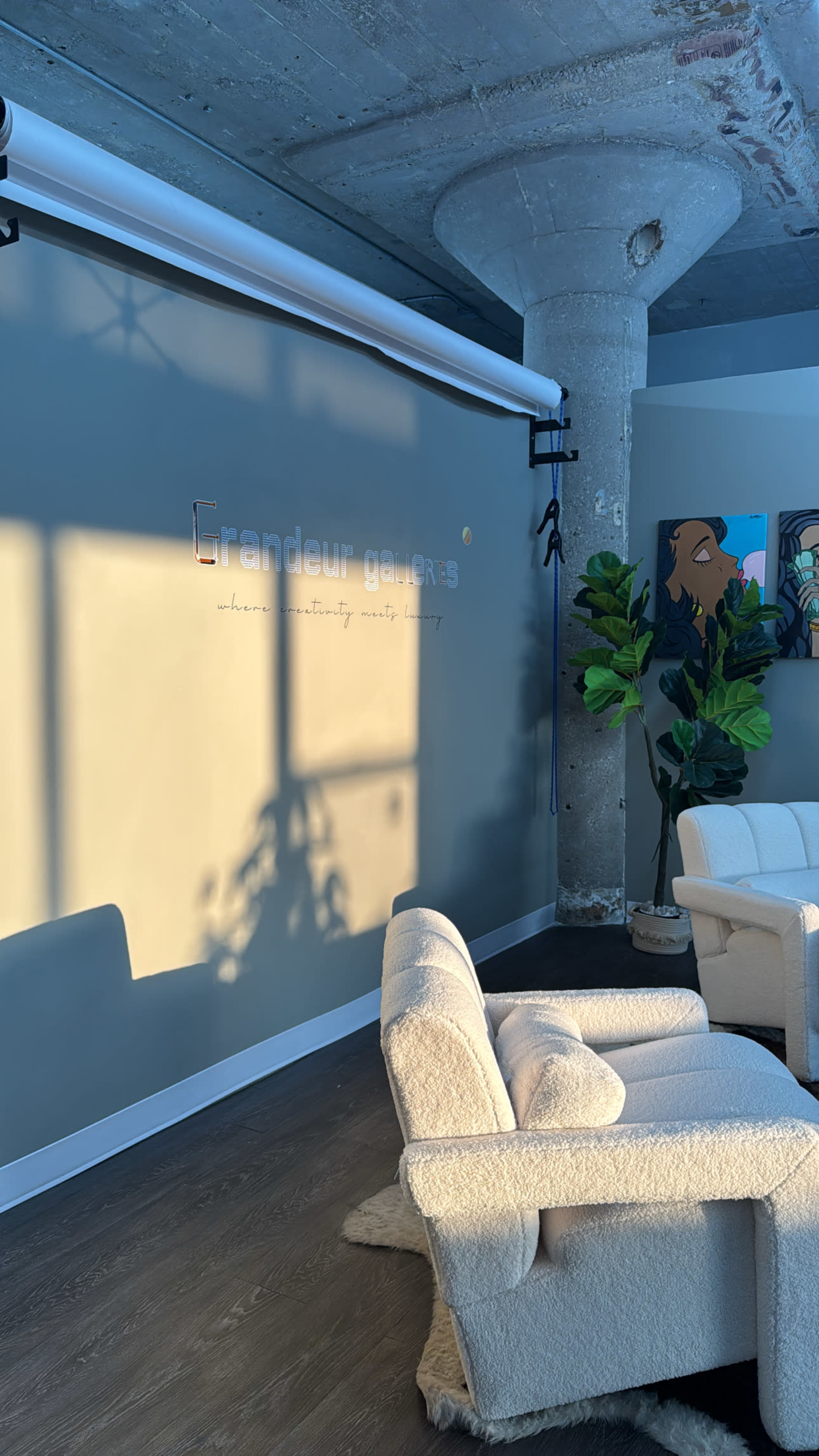 The image shows a modern office space featuring a plush armchair, a large potted plant, and a wall with a sleek sign that reads "Grandeur Gardens."