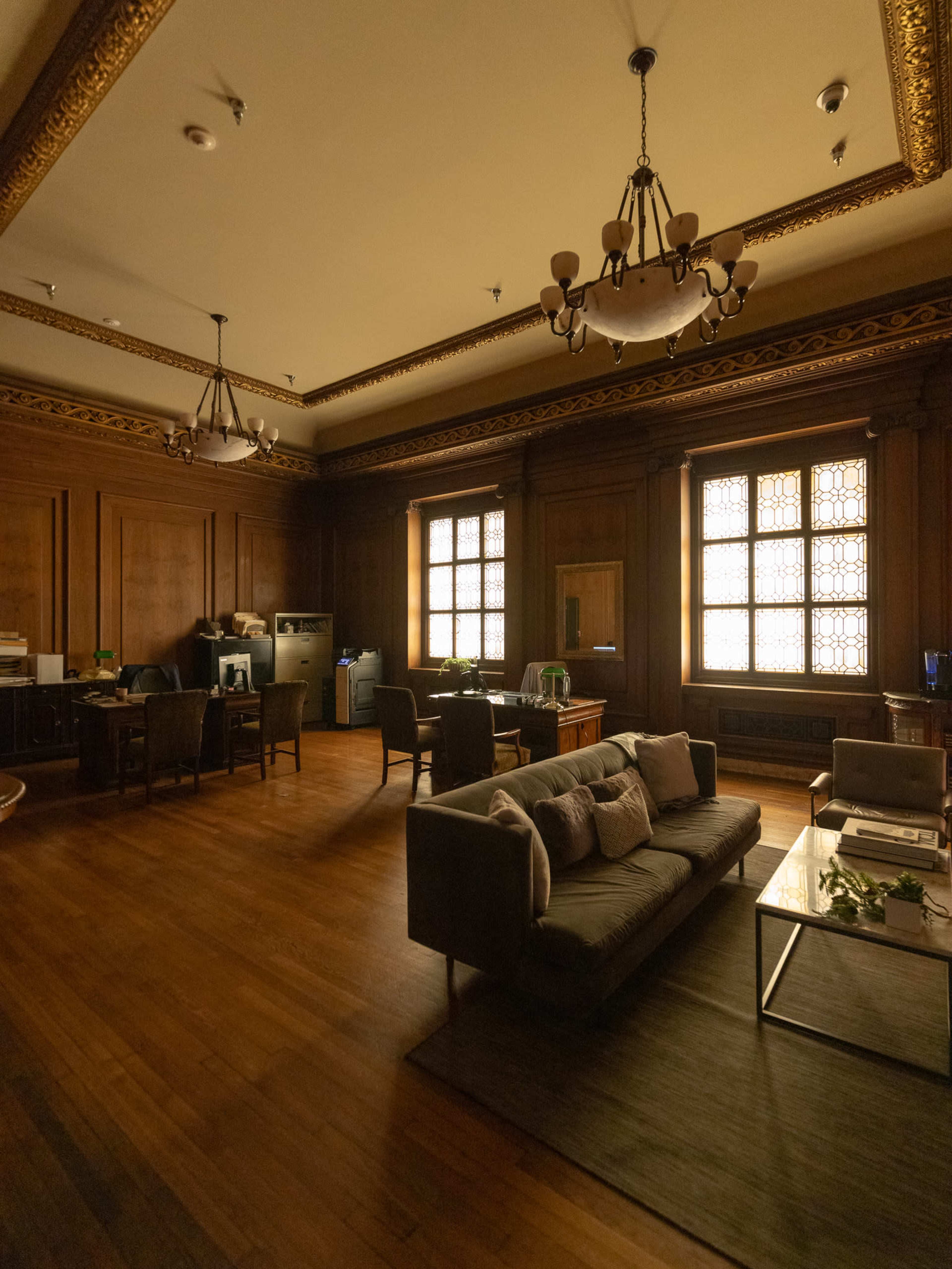 The image shows a spacious, elegantly designed office with wooden walls, a seating area, and large windows allowing natural light to enter.