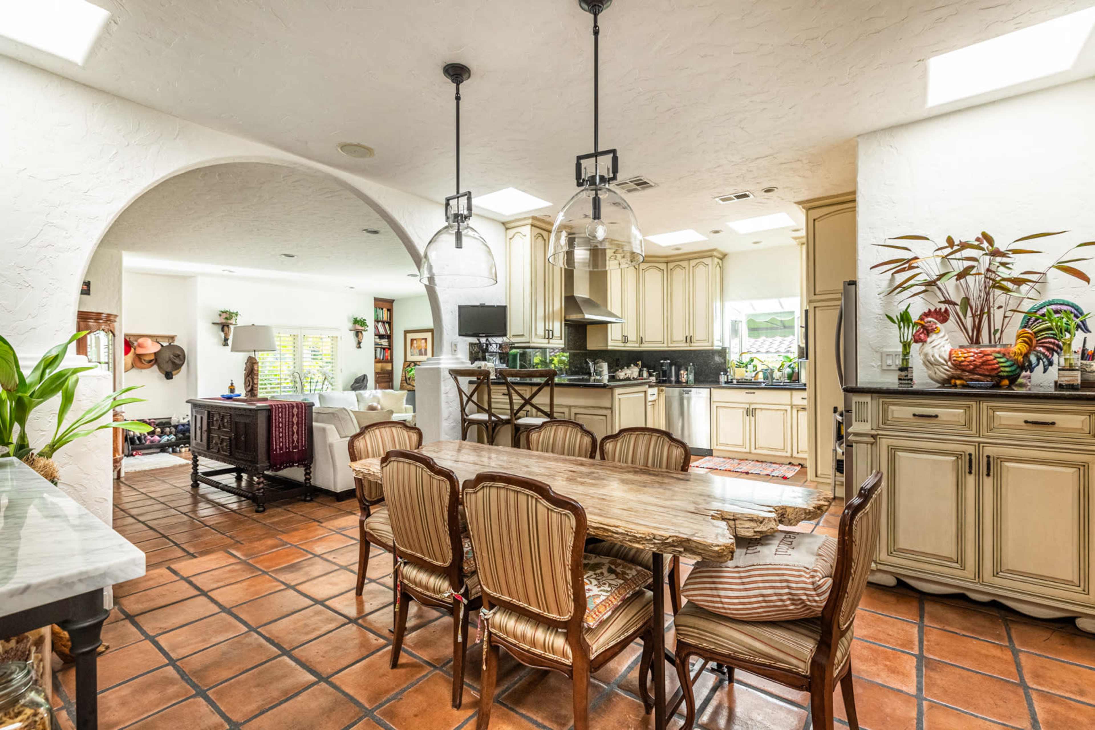 A spacious kitchen and dining area features a large wooden table surrounded by chairs, connected to a well-equipped kitchen through an archway.