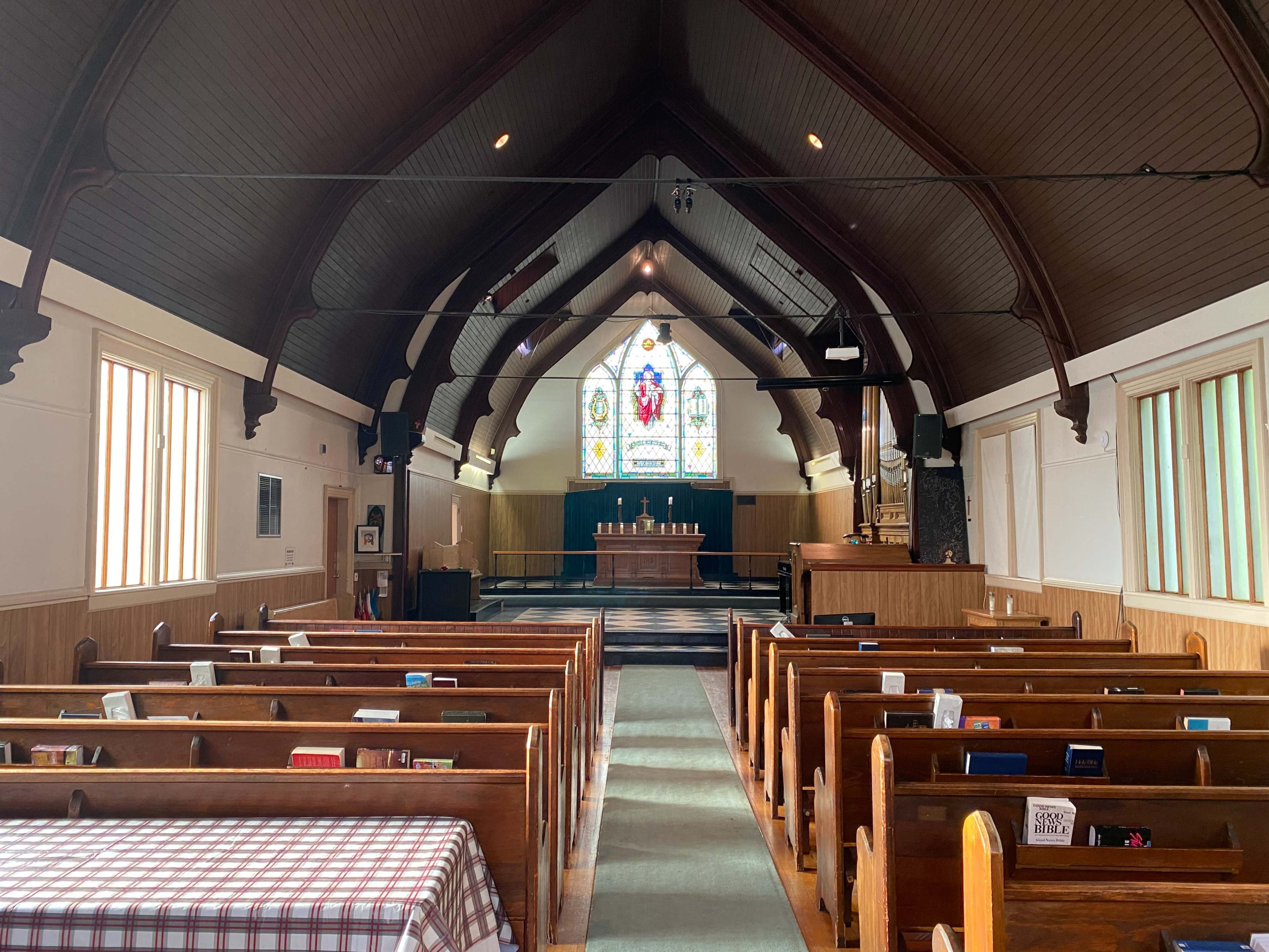 The interior of a church with wooden benches facing an altar and a colorful stained glass window at the end.