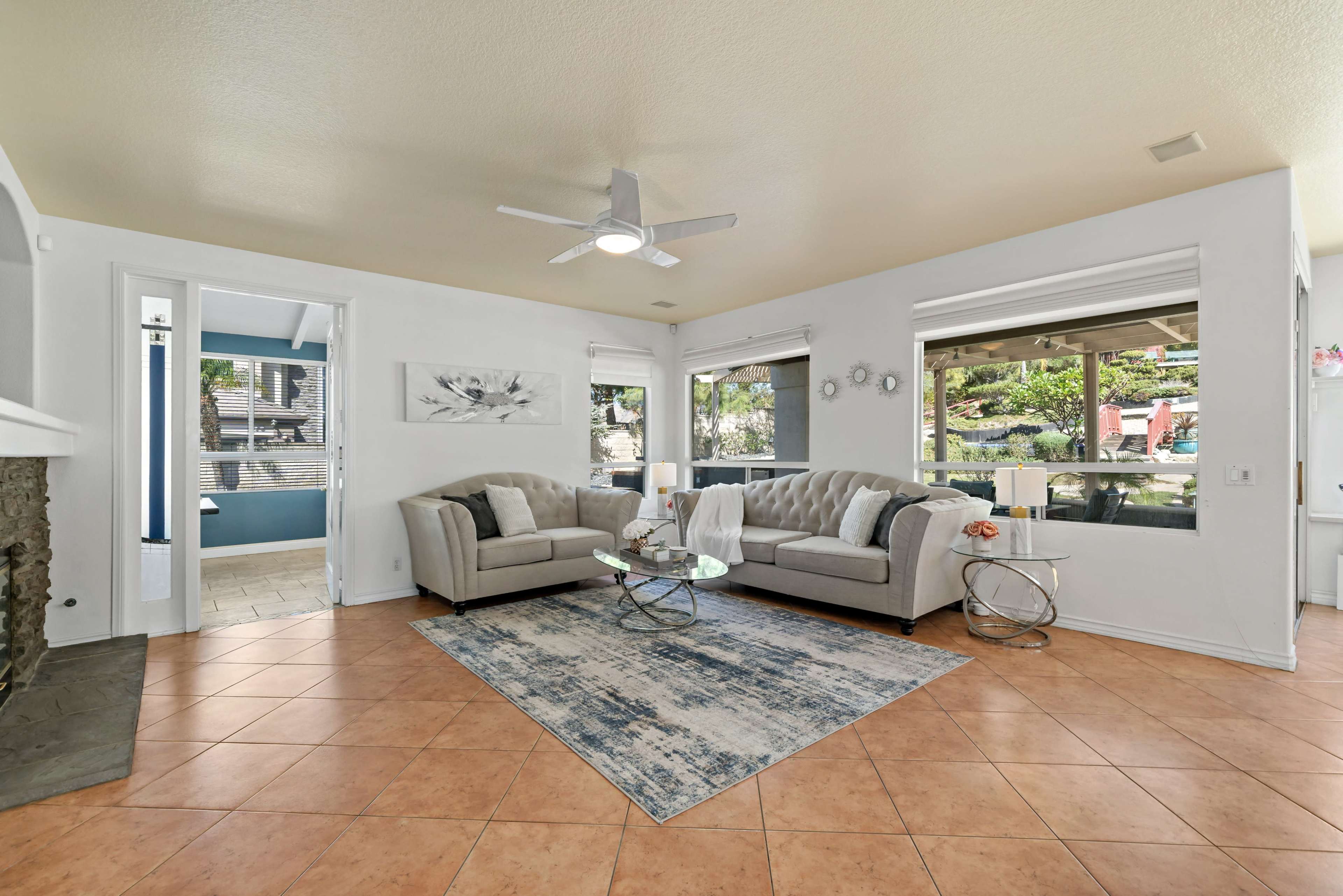 The living room features two gray sofas facing a circular glass coffee table, with large windows allowing natural light to illuminate the space.