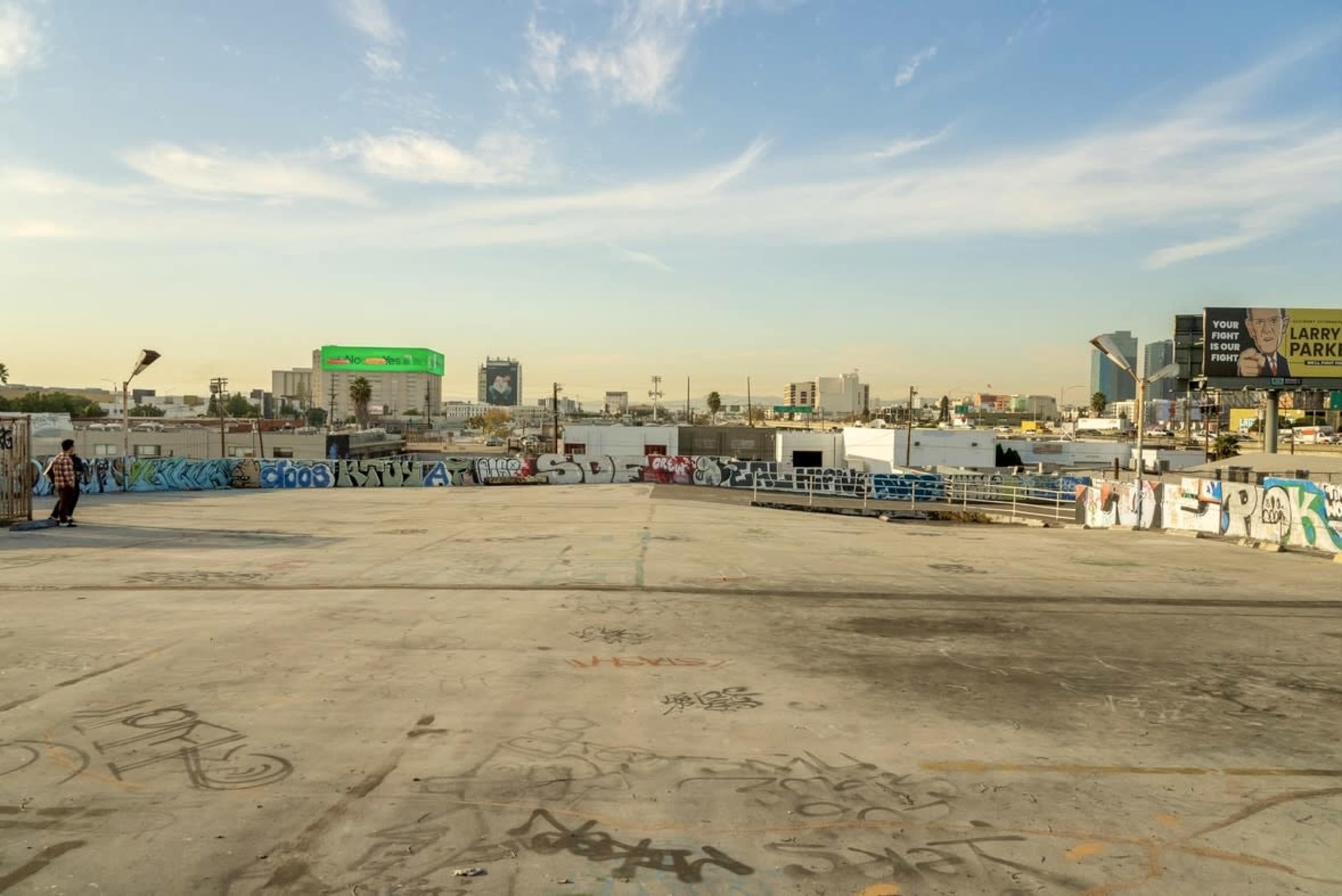 The image shows a graffiti-covered concrete surface with a skyline, including billboards and buildings, visible in the background under a clear sky.
