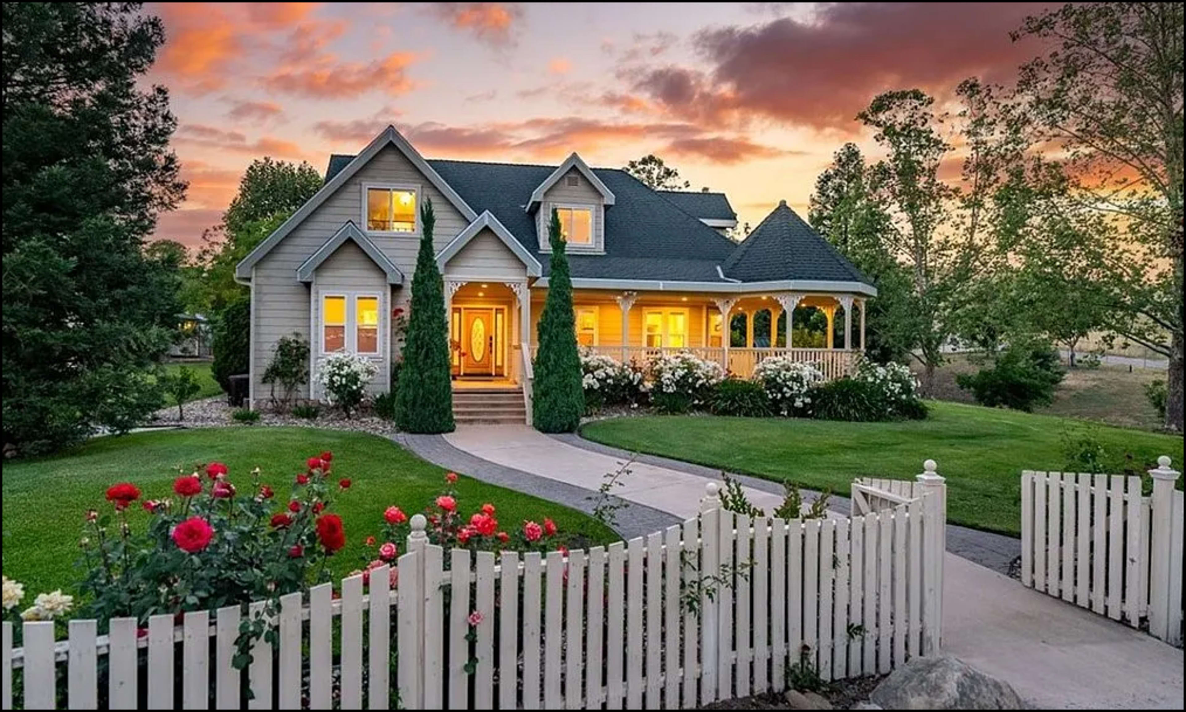 A well-maintained house with a front porch and landscaped yard is set against a vibrant sunset sky.