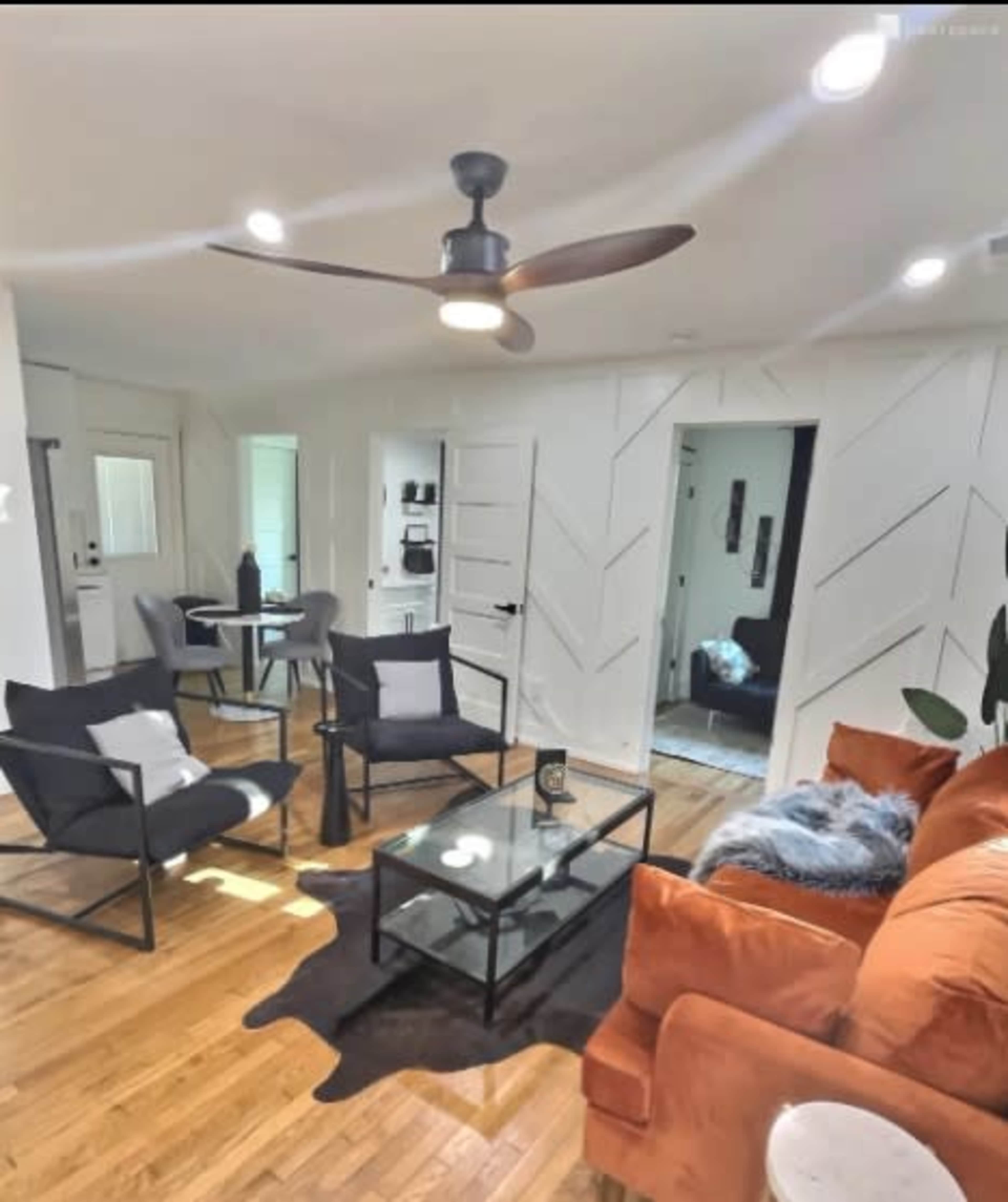 A living area with a mixture of seating options including a sofa, chairs, and a coffee table, all arranged on a hardwood floor.