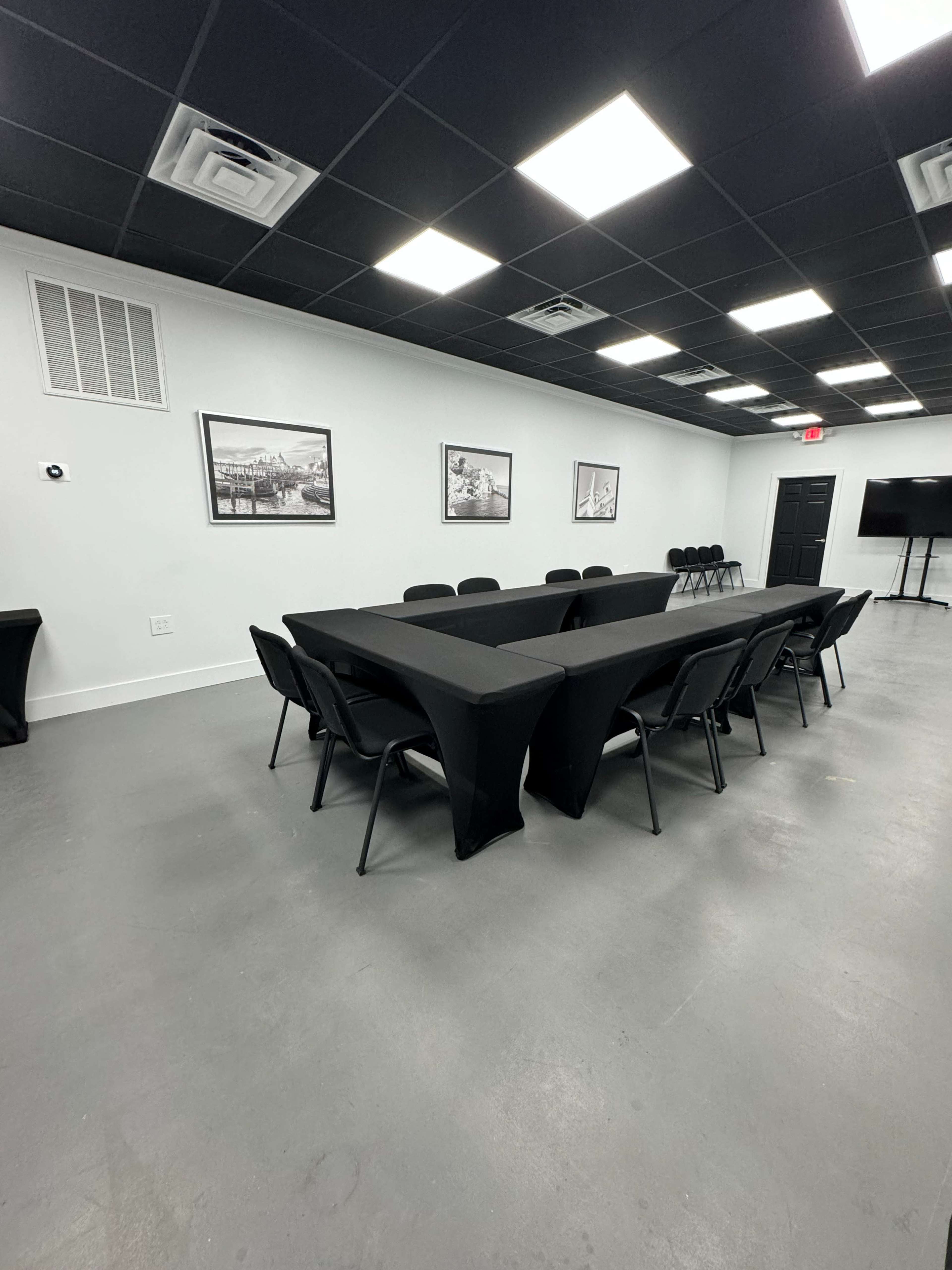 The image shows a conference room with a long black table surrounded by chairs, and several framed pictures hanging on the white walls.