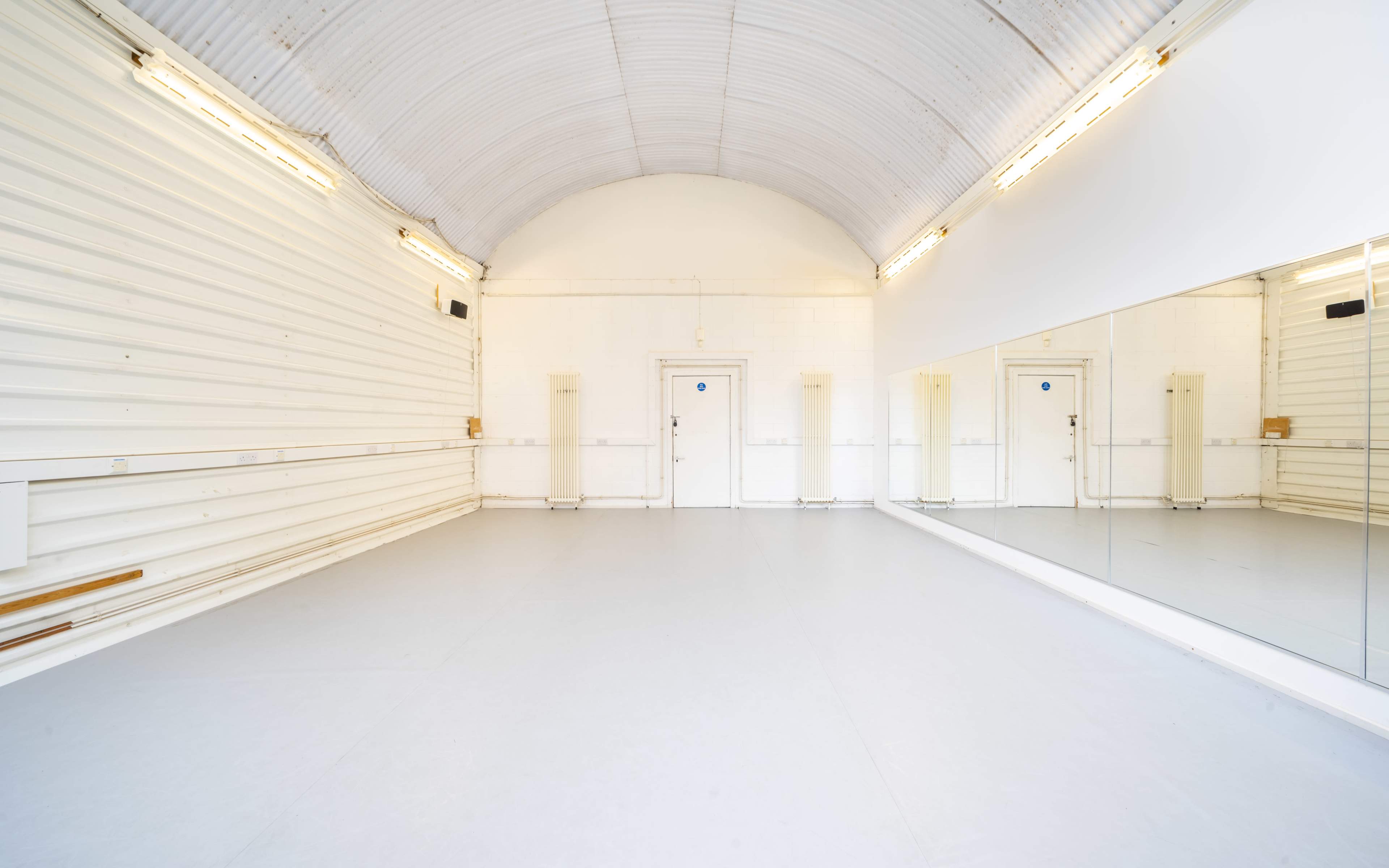 A spacious, empty dance studio with a mirrored wall and two doors at the far end.