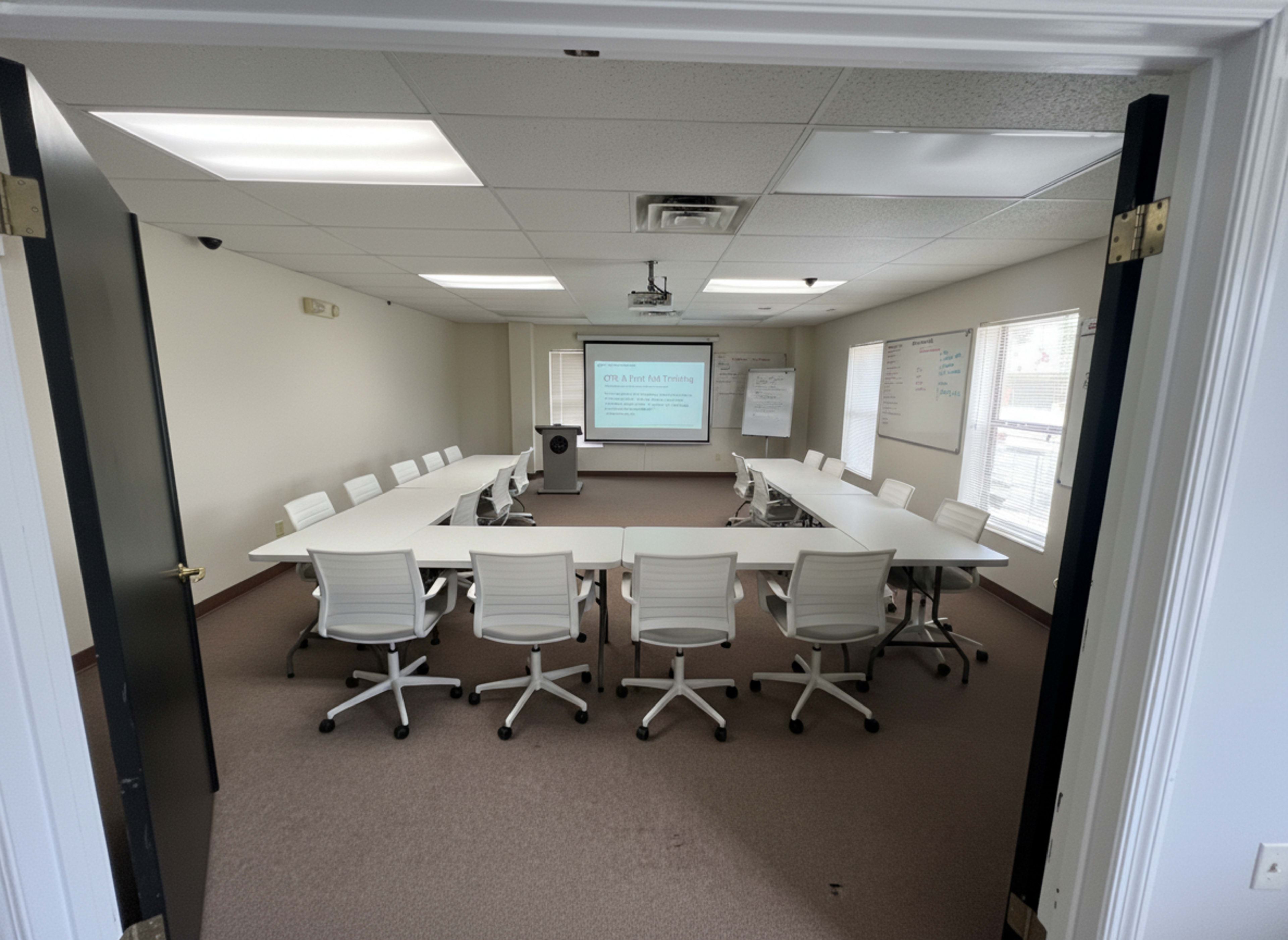 A conference room with a long table surrounded by white chairs and a projector displaying a presentation on a screen at one end.