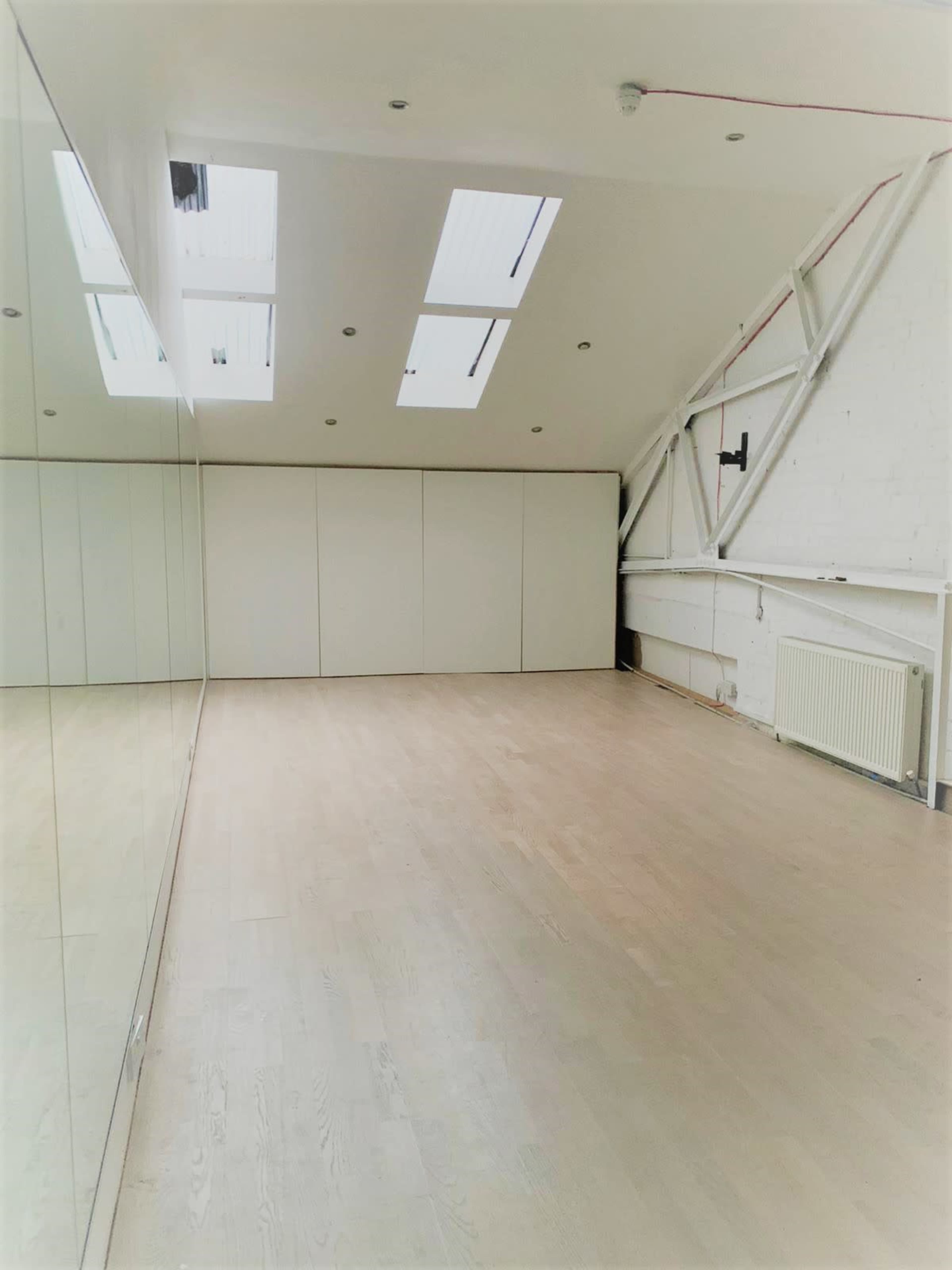 A spacious room with wooden flooring, large mirrors on one wall, and skylights above providing natural light.