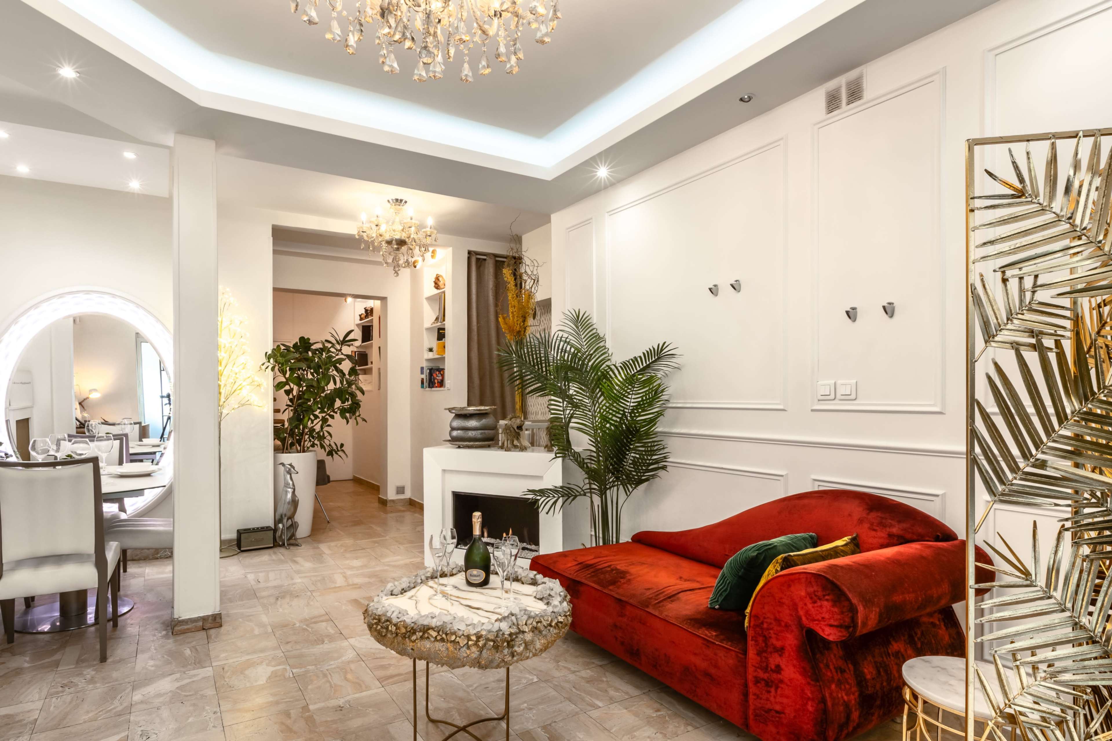 The image features a stylish living room with a red velvet sofa, a marble coffee table, and elegant lighting fixtures, including a chandelier.