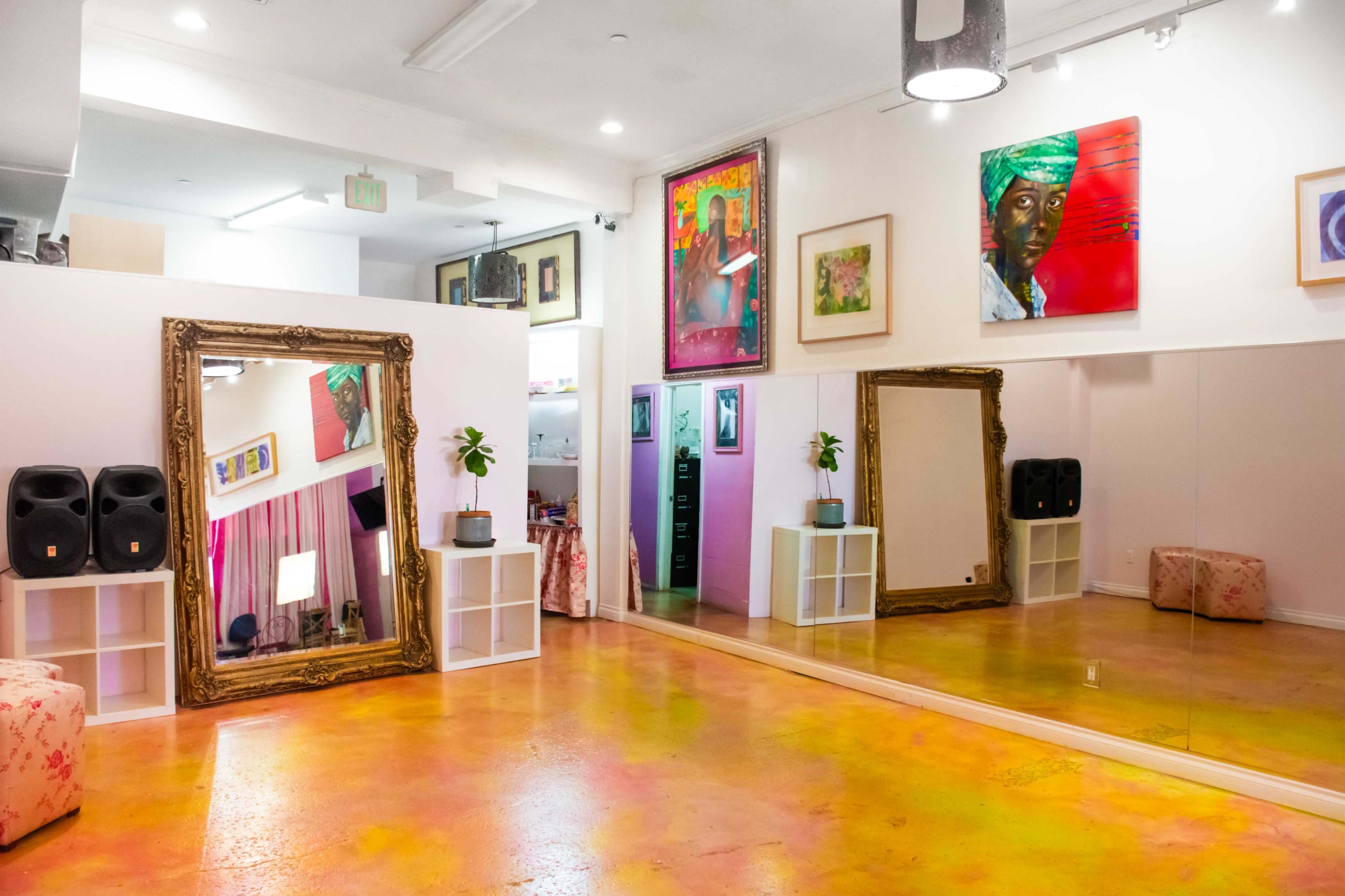 The image shows a brightly lit studio space with mirrors, artwork on the walls, and a polished floor.