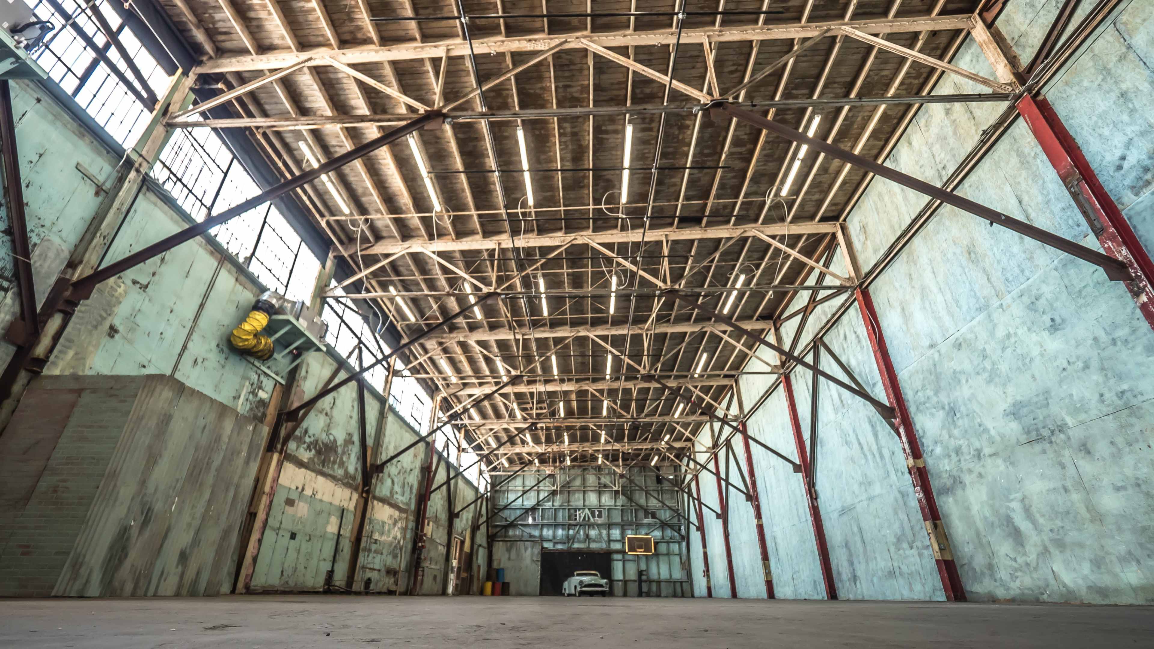 The image shows a large, empty warehouse with tall ceilings supported by metal beams and bare walls.