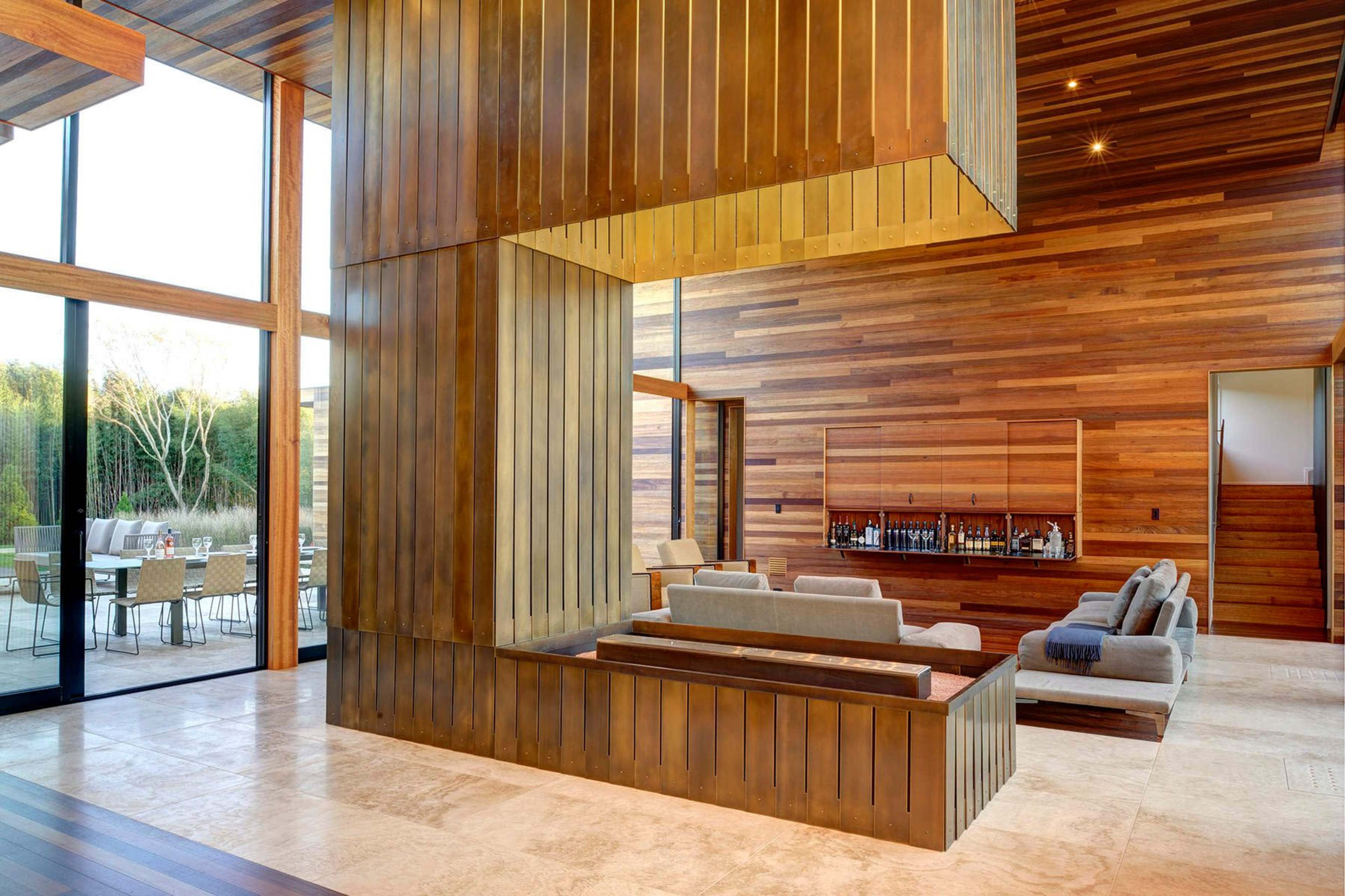 The interior features a spacious lounge area with wooden walls and a central metallic structure, creating a modern aesthetic.