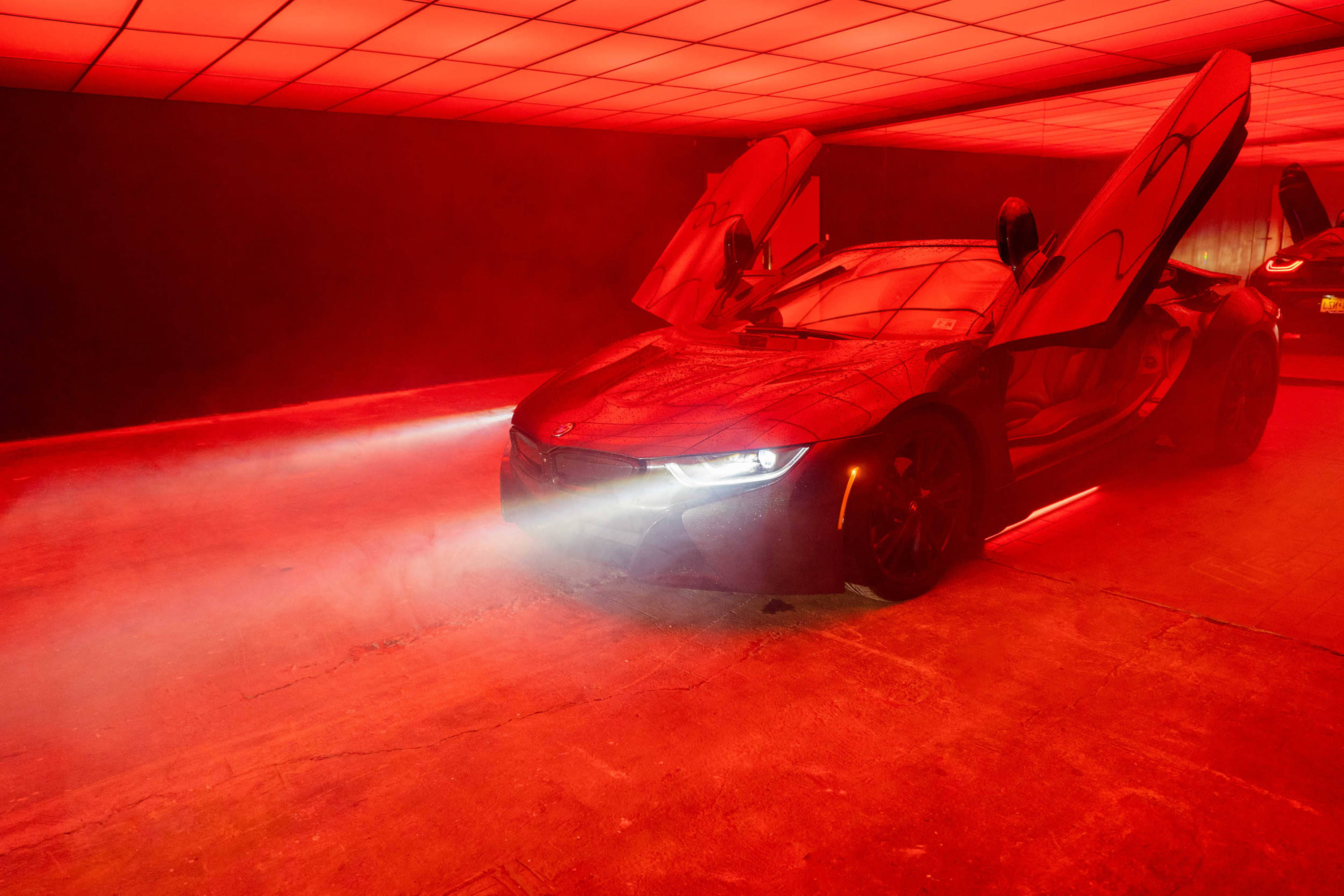 A black BMW i8 sports car with its doors open is illuminated by red lighting in an industrial space.