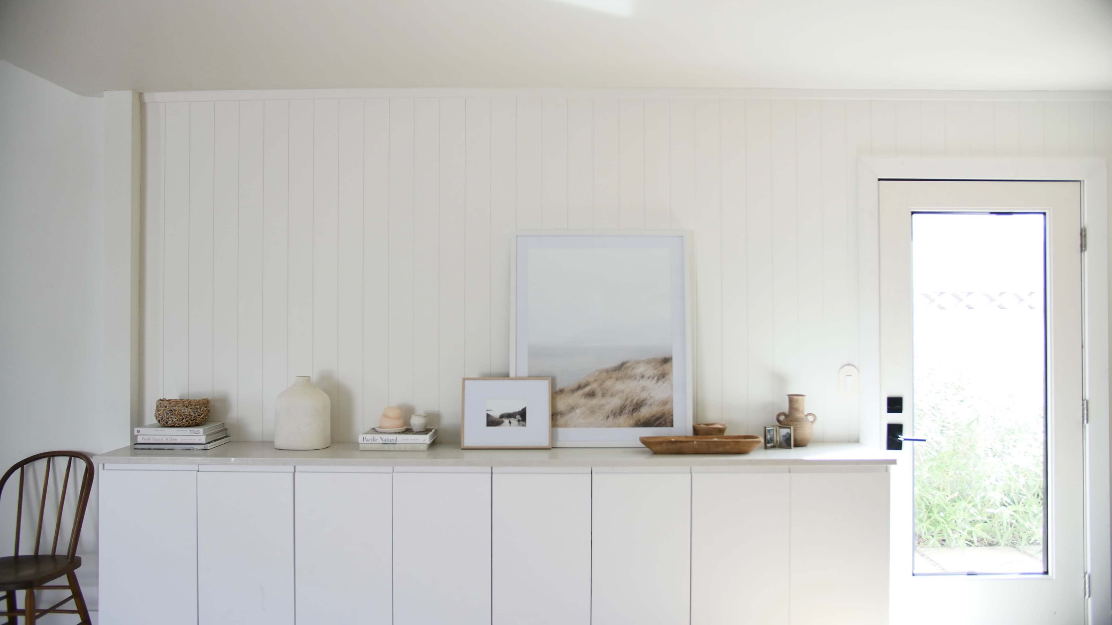 A white-paneled wall with a cabinet displaying decorative items, including a framed picture, a vase, and a bowl, beside a door.