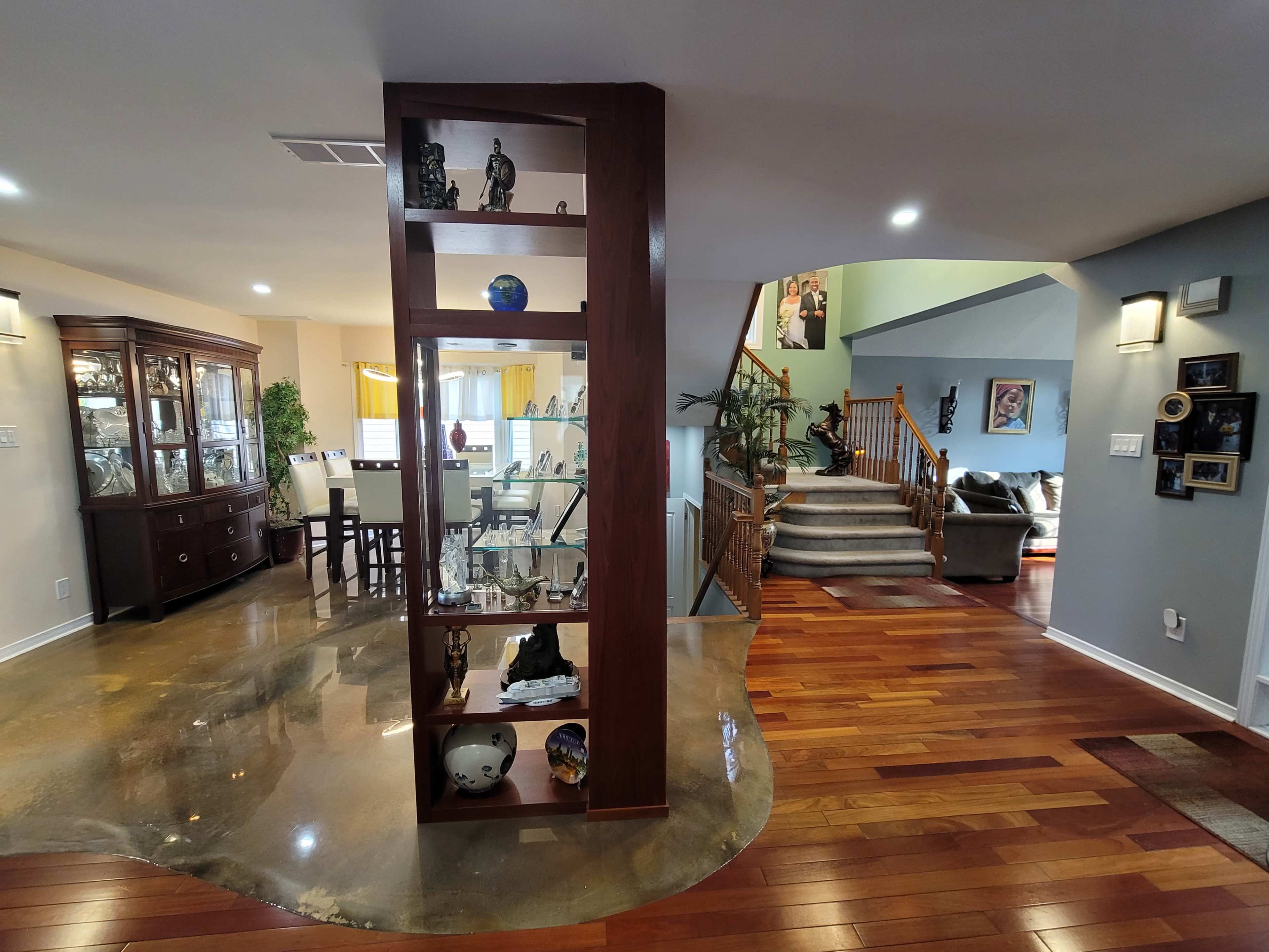 A split-level foyer featuring a display shelf and hardwood flooring, with a dining area visible on the left and a staircase leading to an upper level on the right.