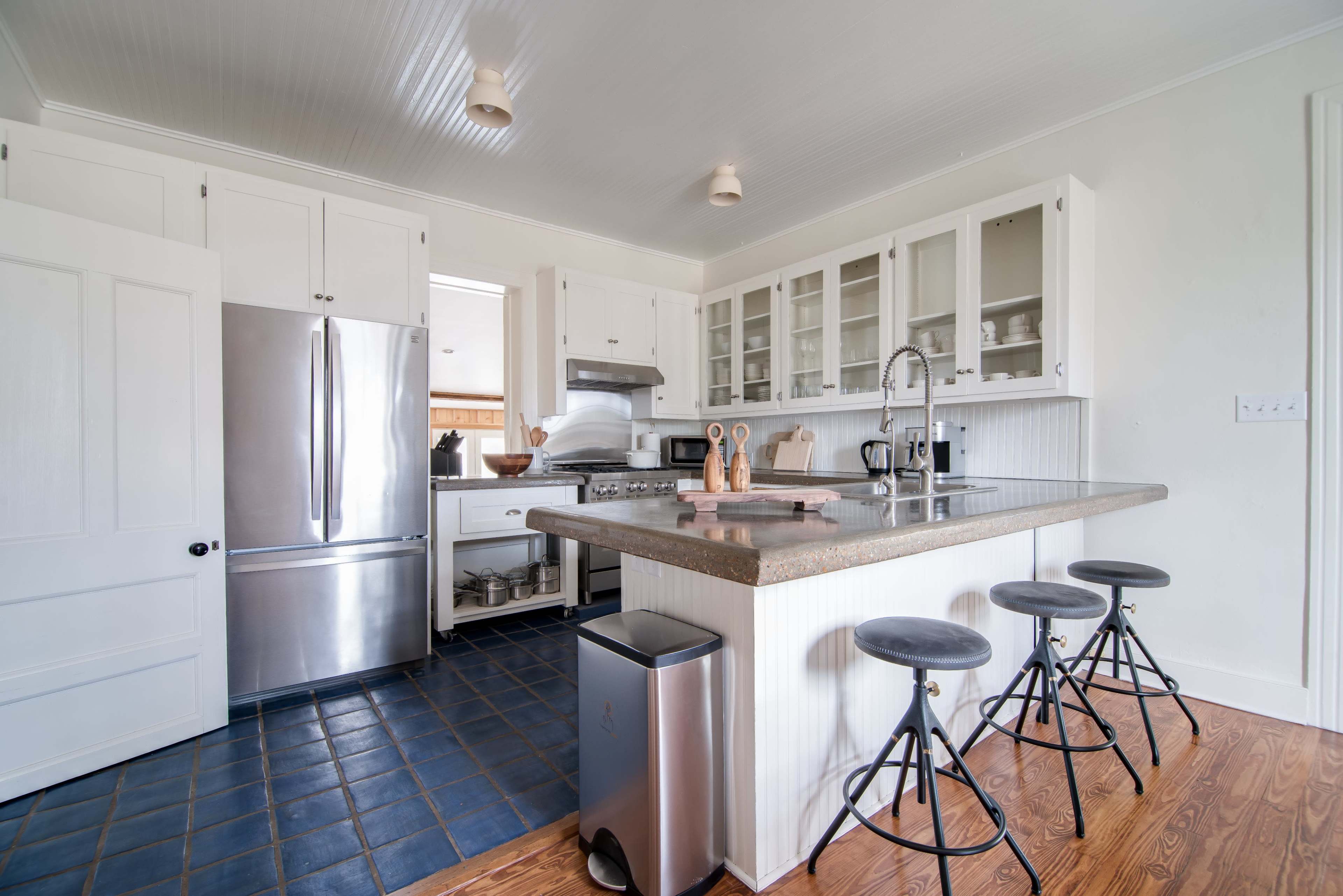 A modern kitchen features a central island with three stools, stainless steel appliances, and white cabinetry.