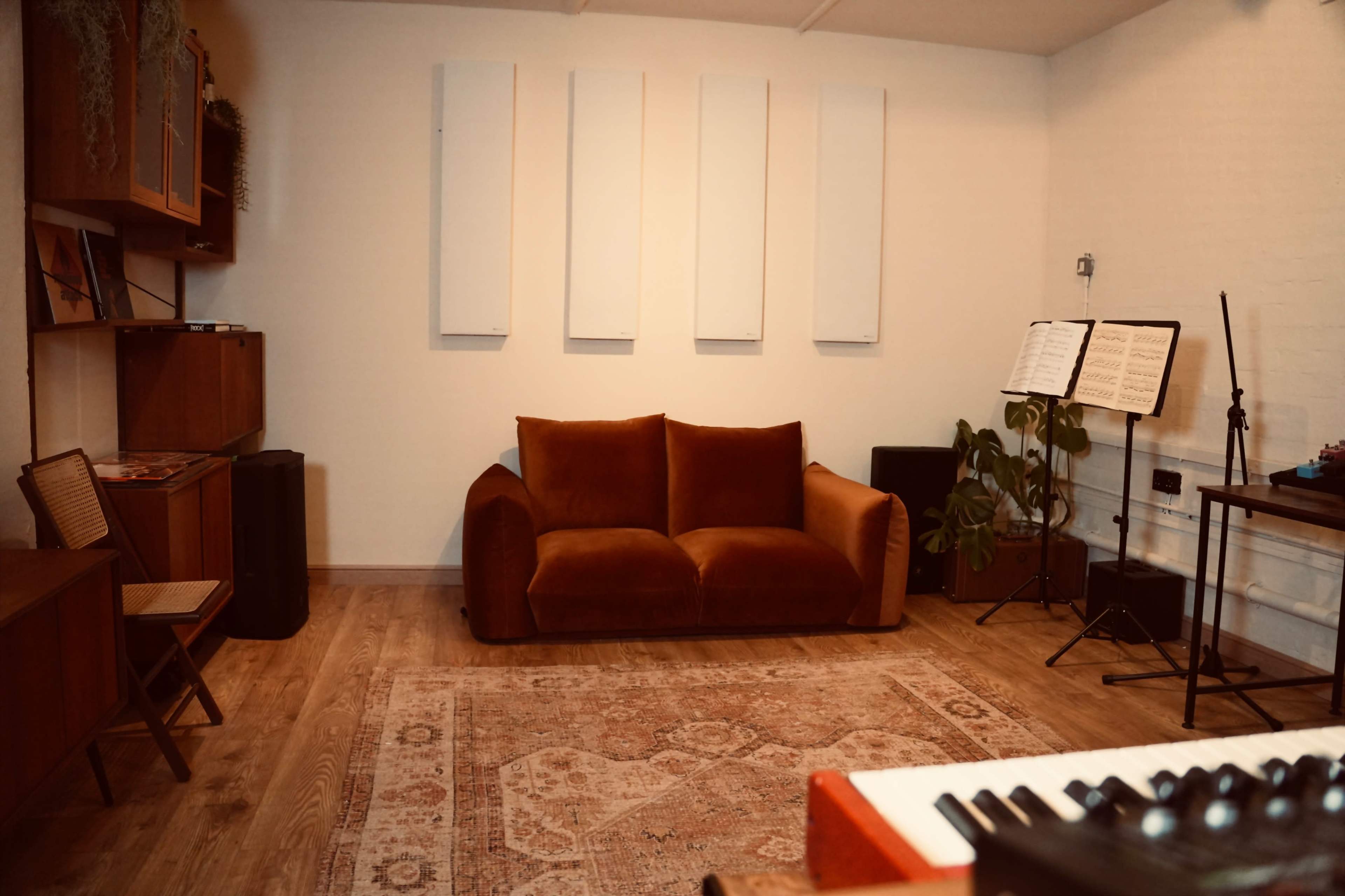The image shows a room with a brown couch, placed on a patterned rug, surrounded by wooden furniture and music stands.