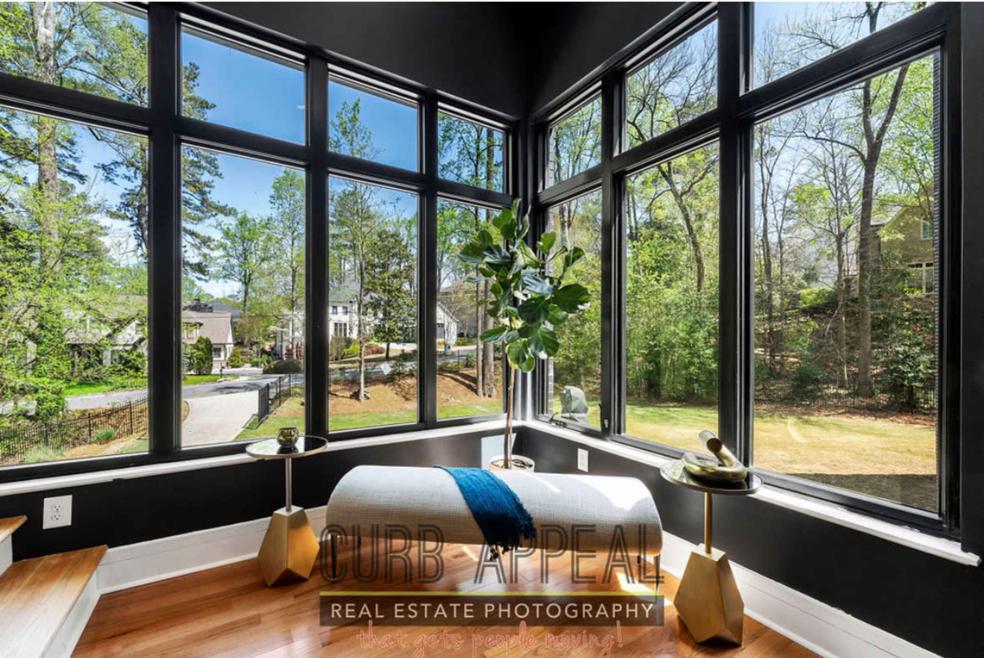 A bright sitting area features large windows with views of a tree-lined street and a decorative bench with a blue throw.