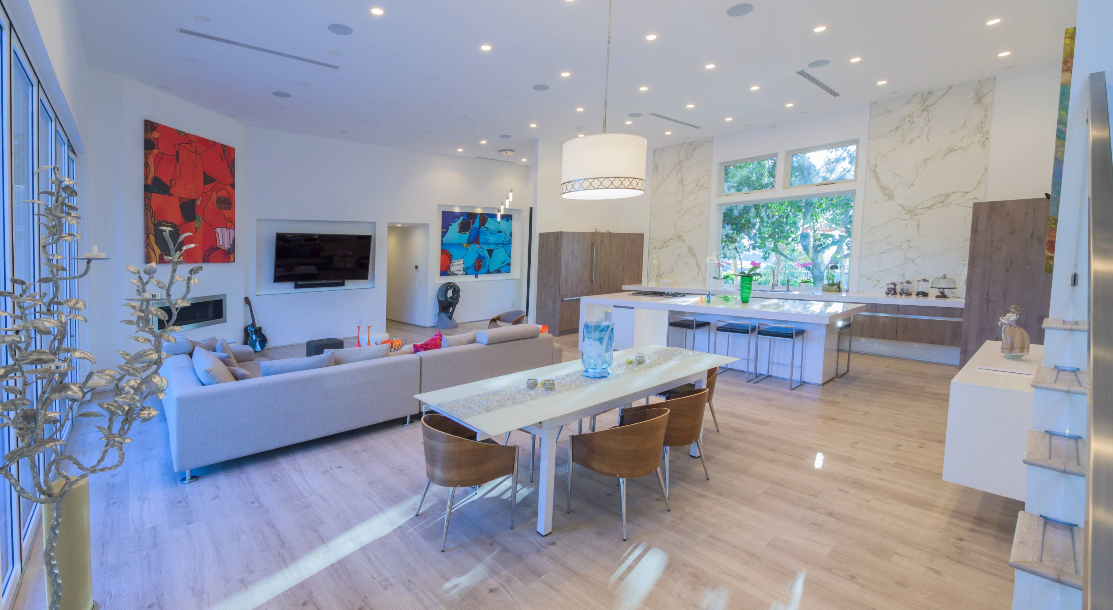 A modern open-concept living and dining area with a large kitchen island, wooden dining chairs, and large windows that let in natural light.