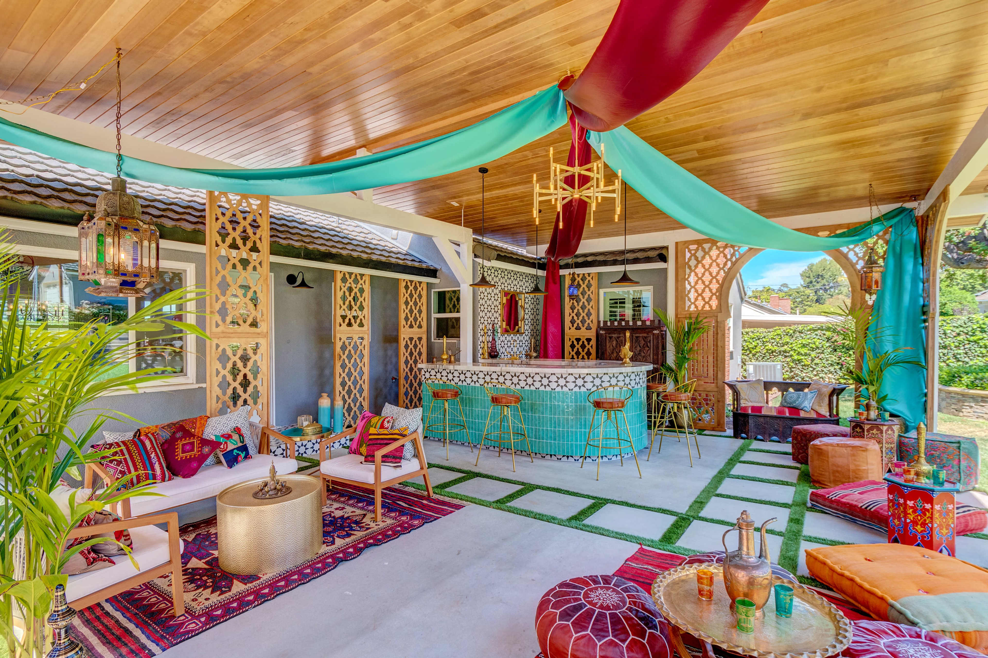 A vibrant outdoor lounge area decorated with colorful textiles and lanterns, featuring a bar and seating arrangements under a canopy.