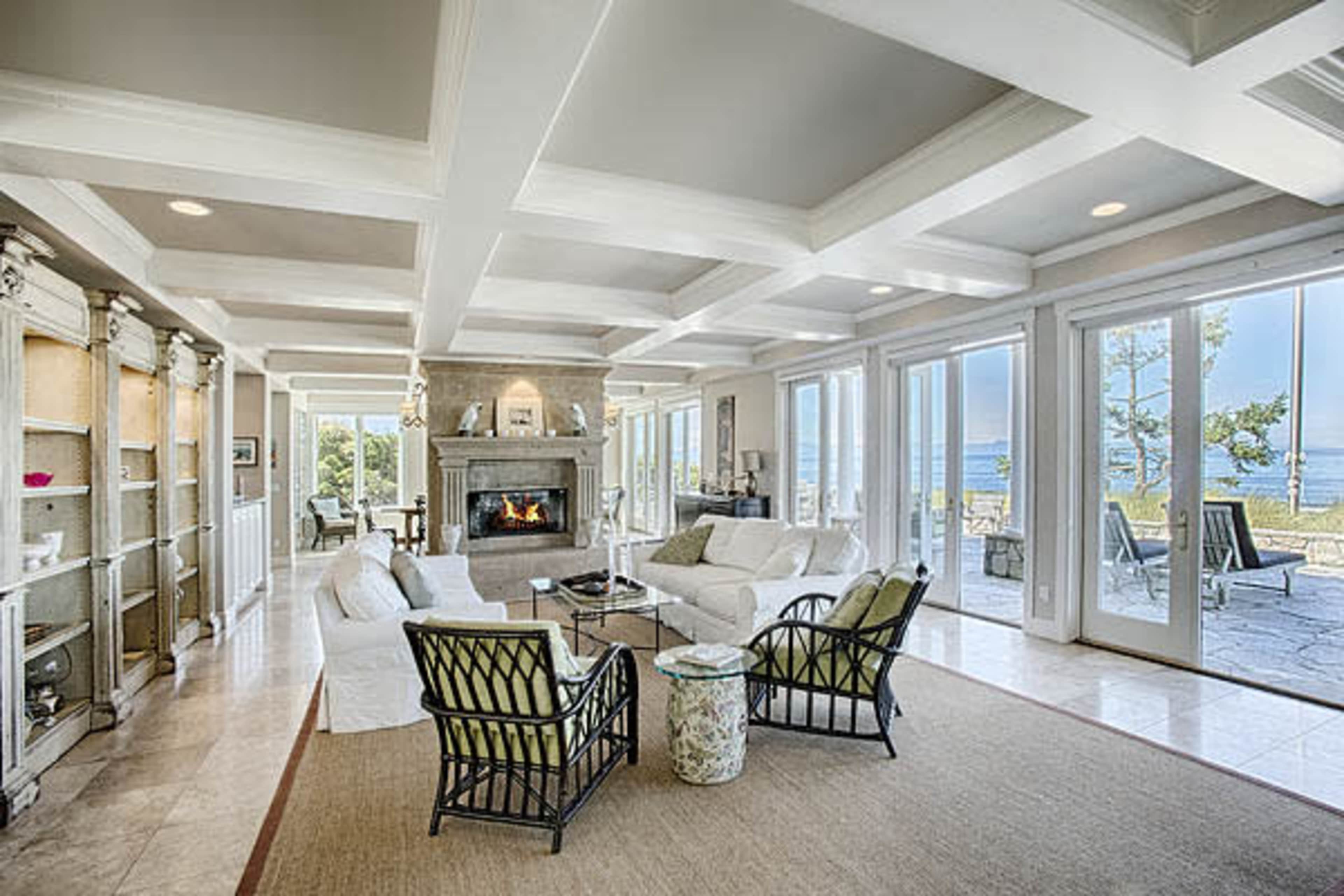 A spacious living room with a fireplace, large windows overlooking a view, and comfortable seating arranged around a coffee table.