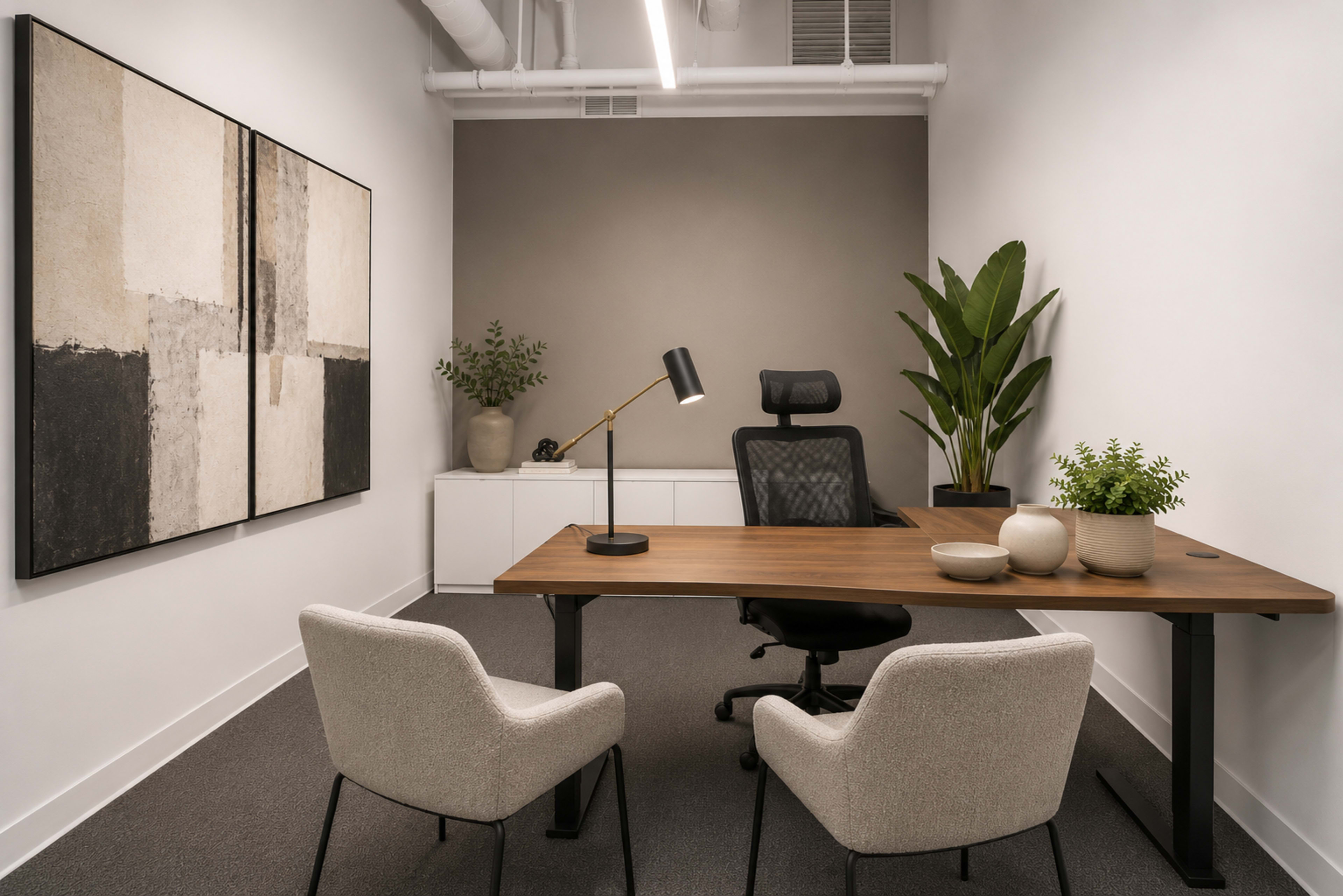 The image shows a modern office space with a wooden desk, a chair, two upholstered armchairs, a decorative wall painting, and potted plants.