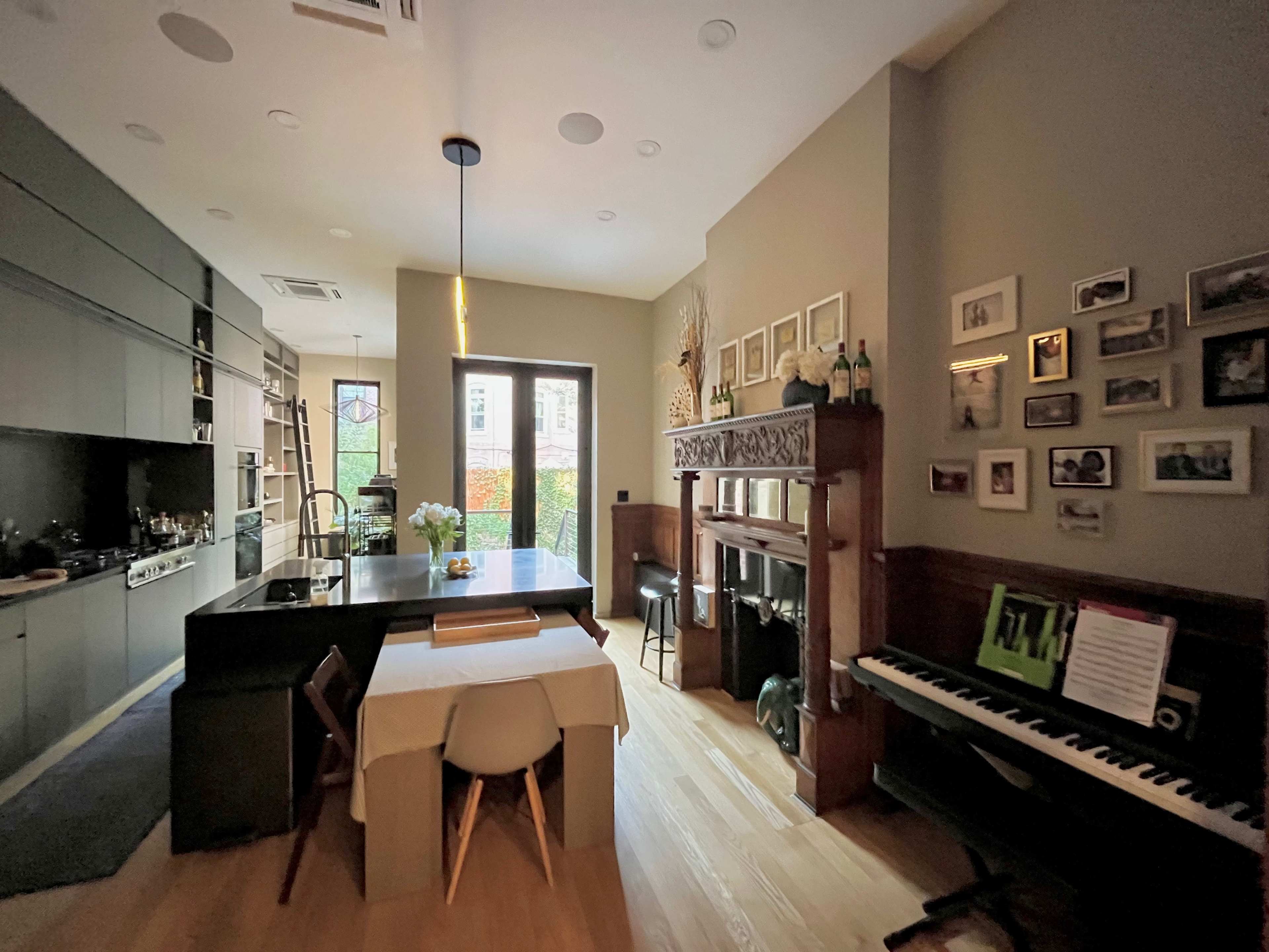 A modern kitchen and dining area with a fireplace and a piano against the wall, featuring a table in the center and cabinets in the background.