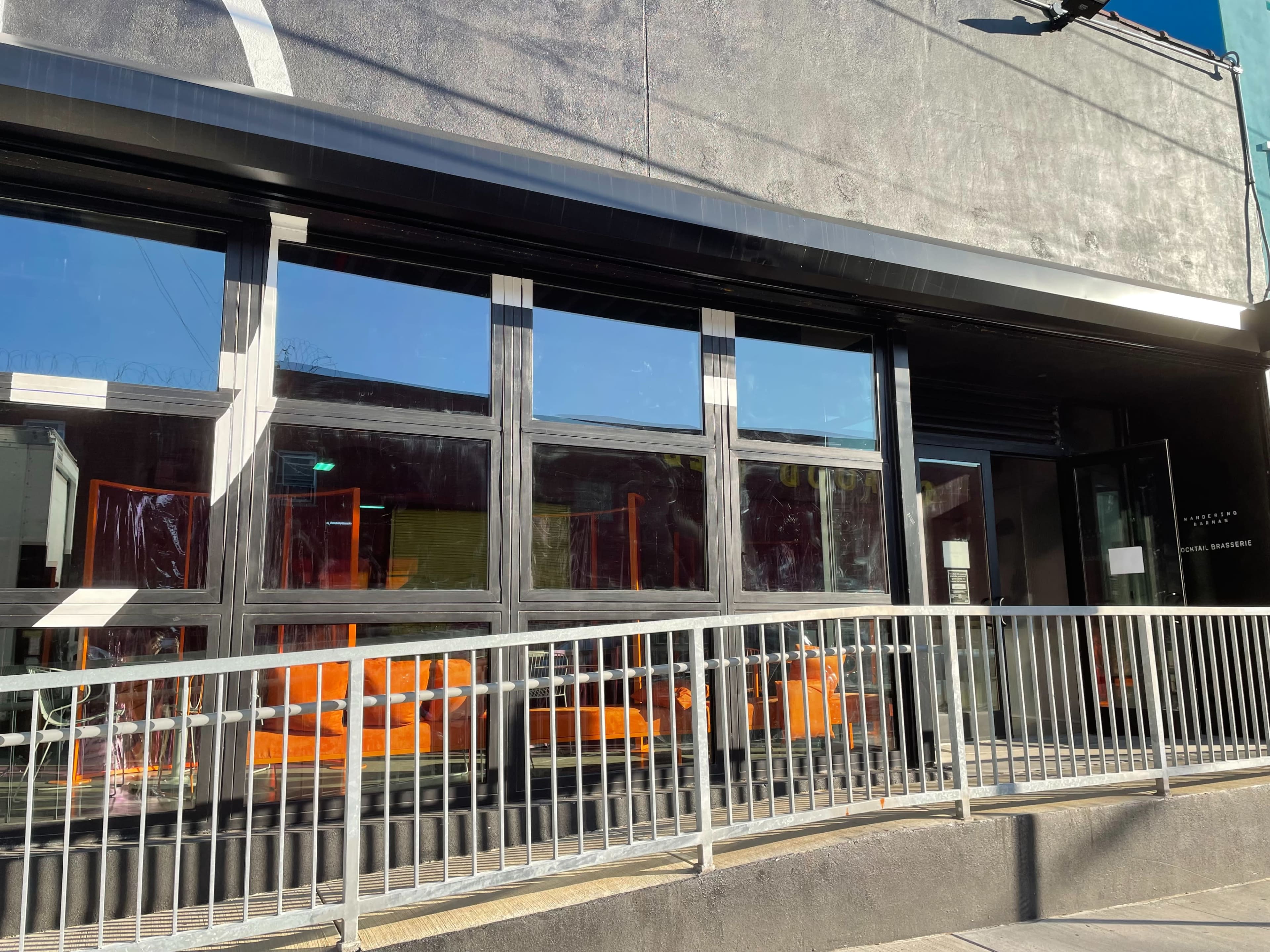 A modern building features large windows with orange decor visible inside and a ramp leading to the entrance.