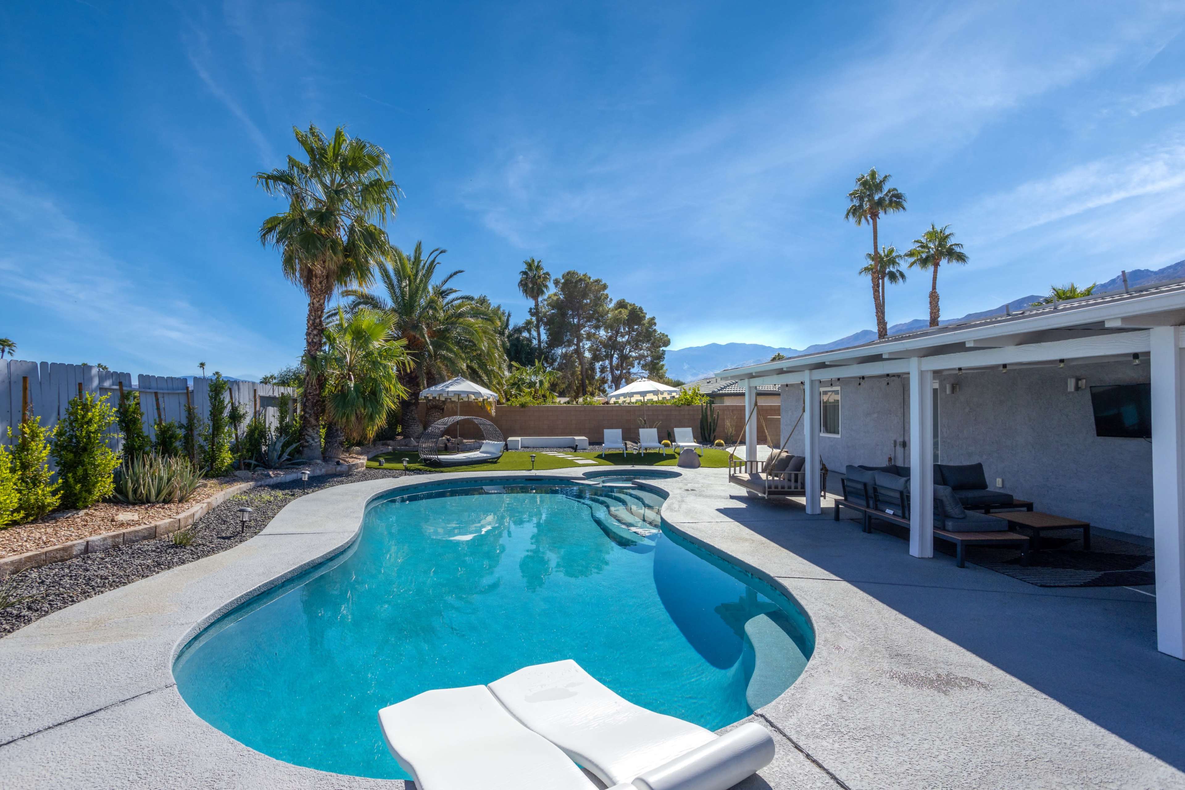A serene backyard with a swimming pool, surrounded by palm trees and lounge chairs under umbrellas.