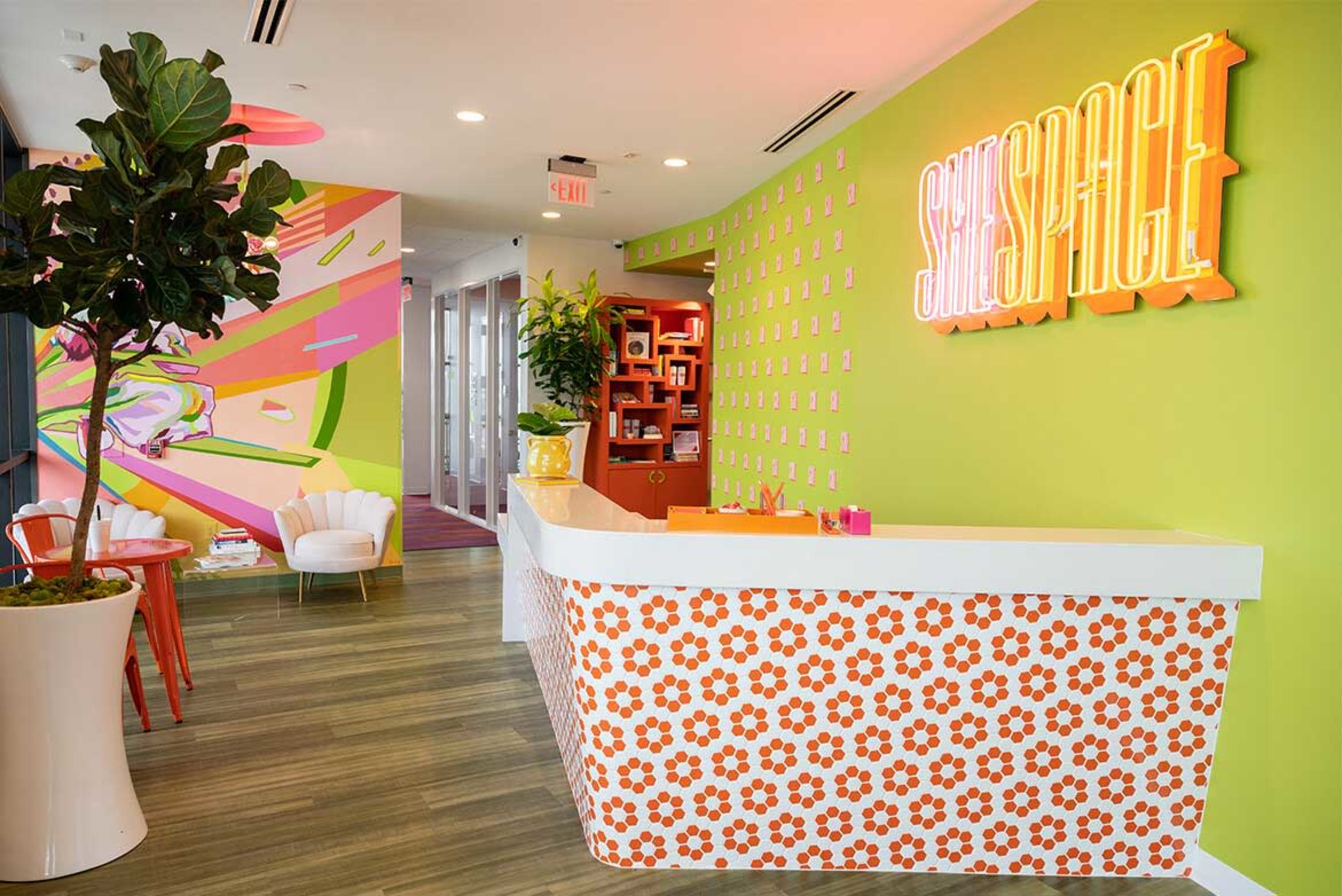 The image shows a brightly colored reception area featuring a floral-patterned front desk, vibrant wall art, and modern seating arrangements.