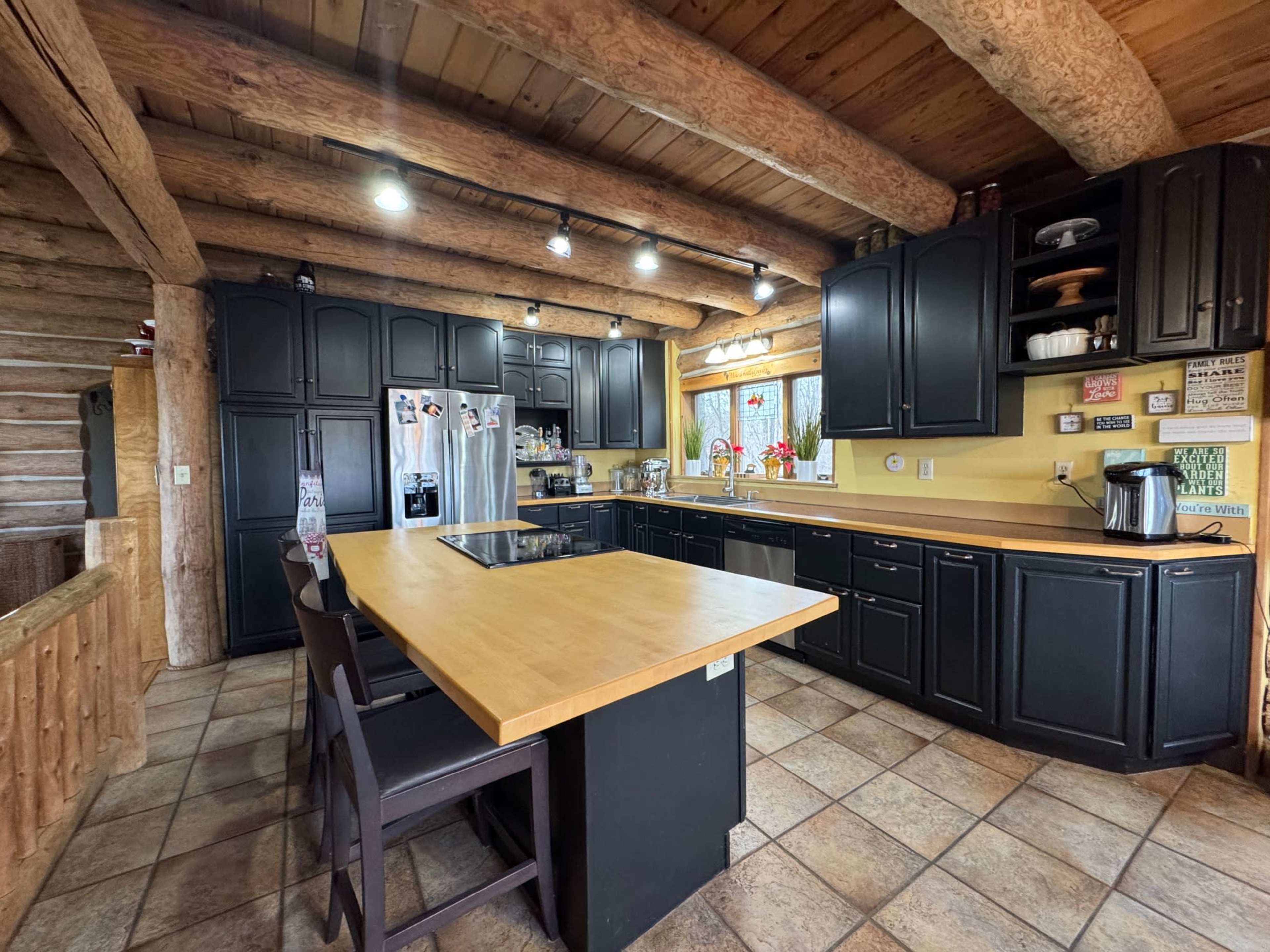 The kitchen features wooden beams overhead, black cabinetry, a central island with seating, and stainless steel appliances.