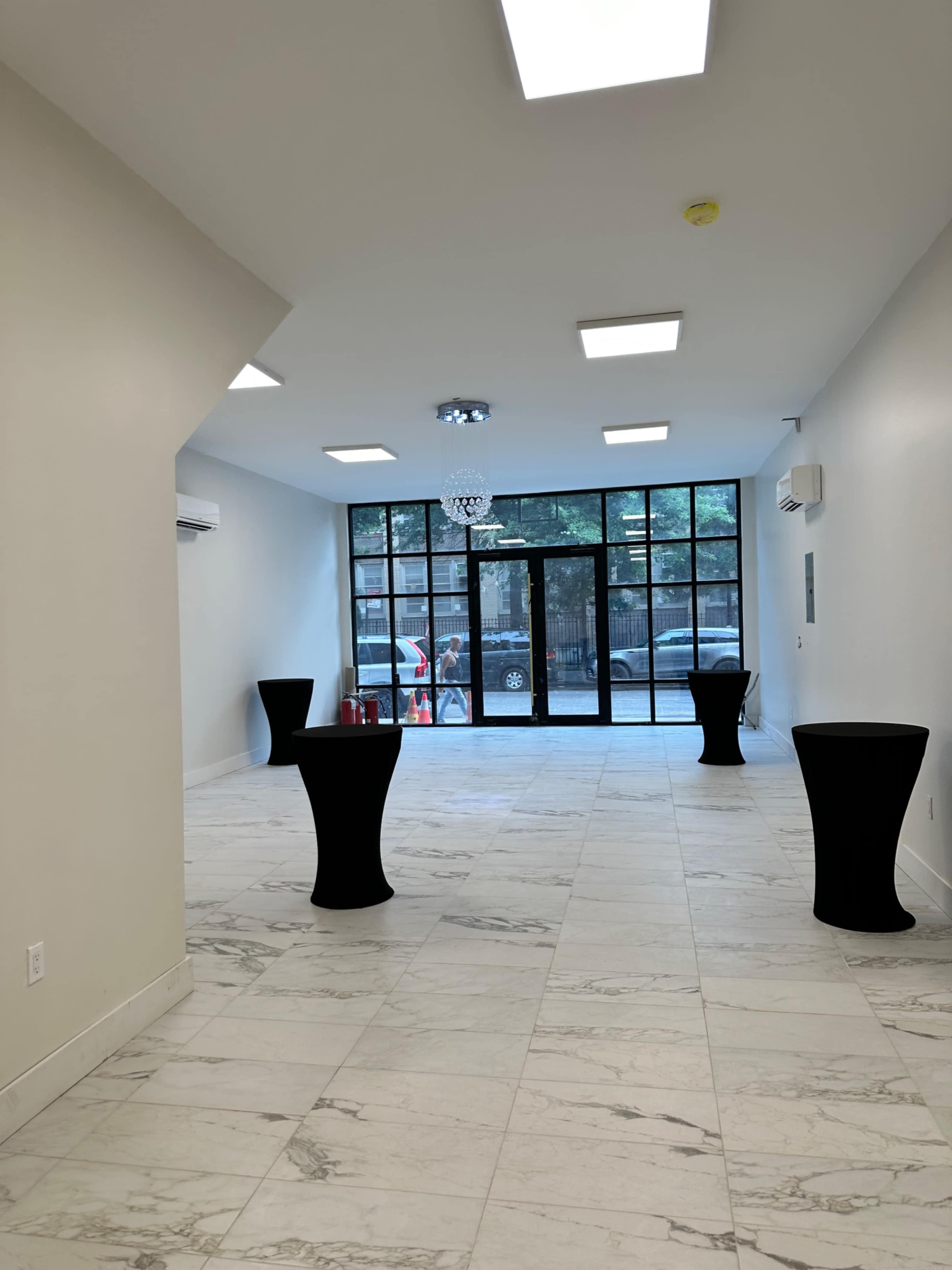 A spacious, well-lit interior with polished marble floors, large windows, and two tall black tables.