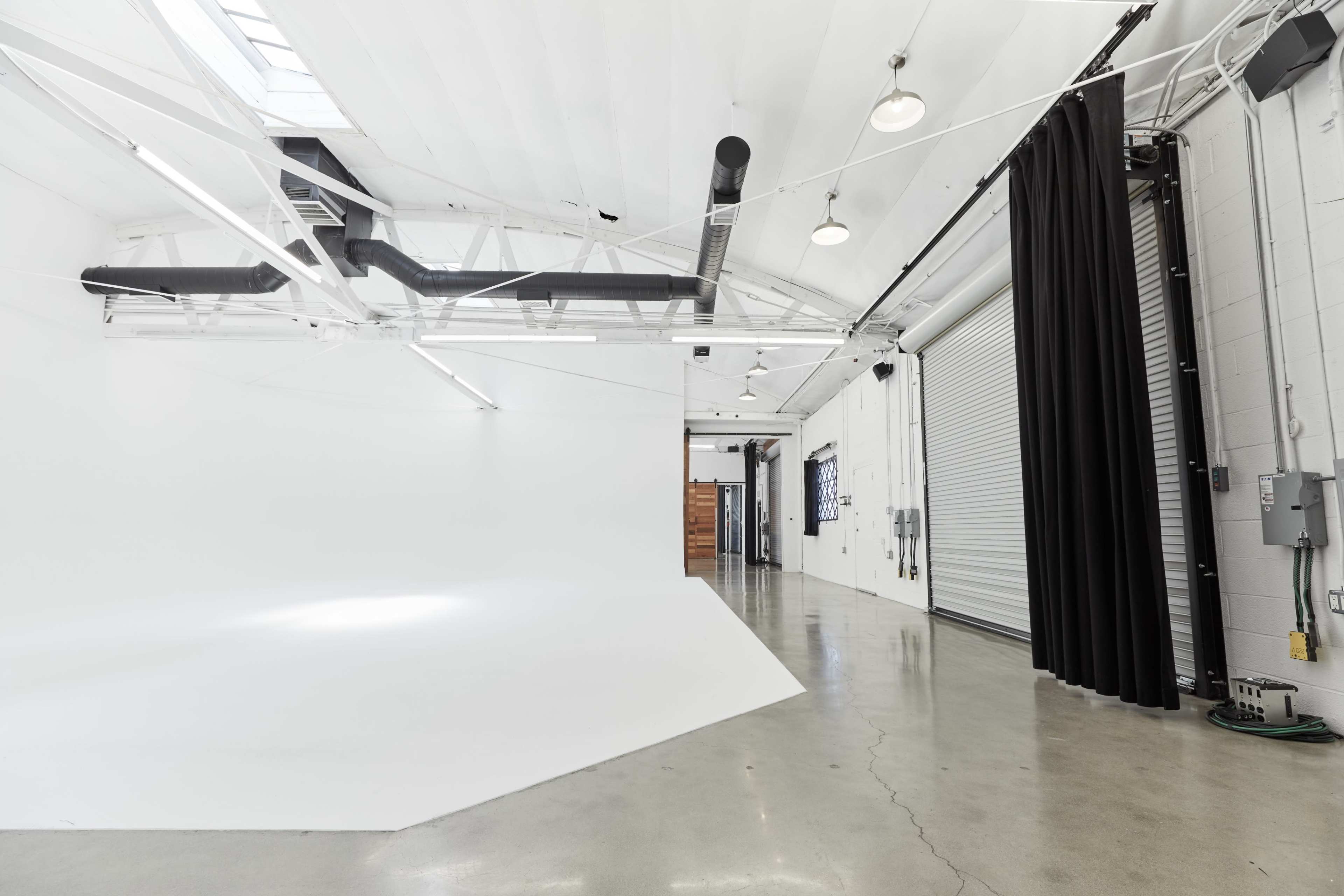 The image shows a spacious, well-lit studio with a white seamless backdrop, polished concrete flooring, and overhead lighting.
