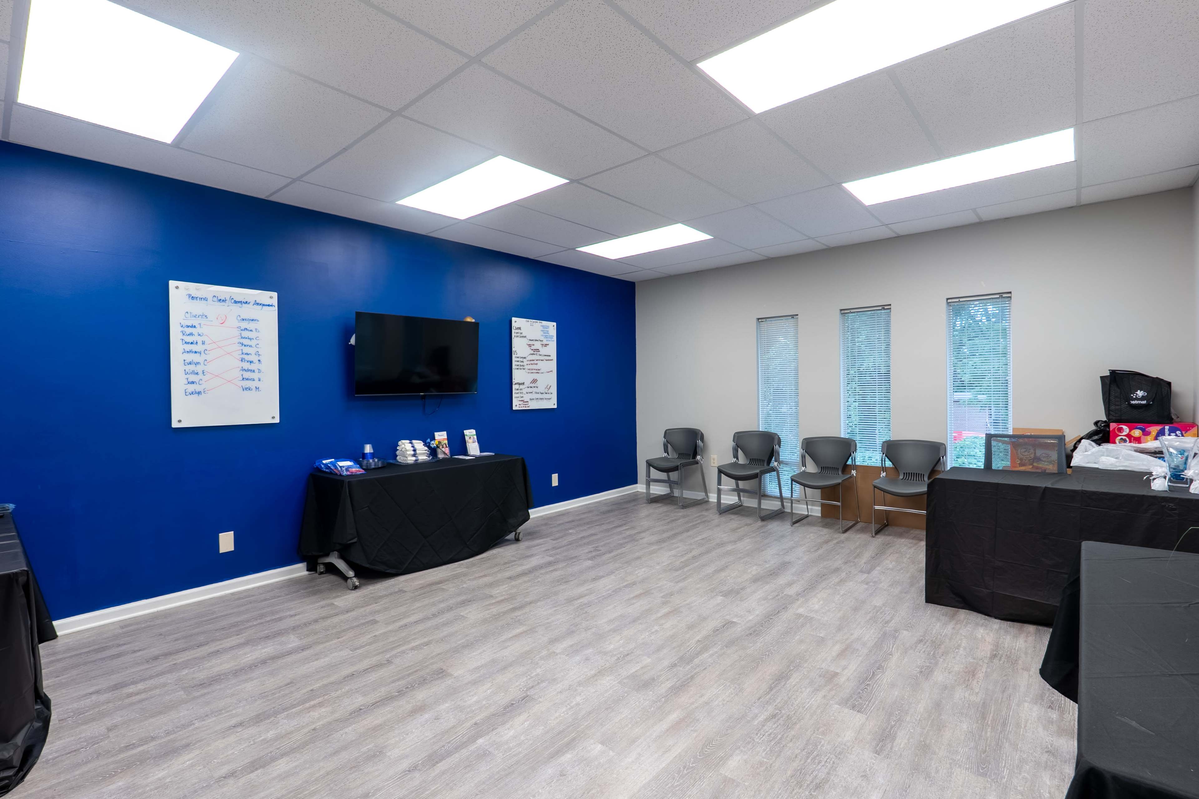The image shows a large room with a blue accent wall, a television, several chairs, and tables displaying items along one side.
