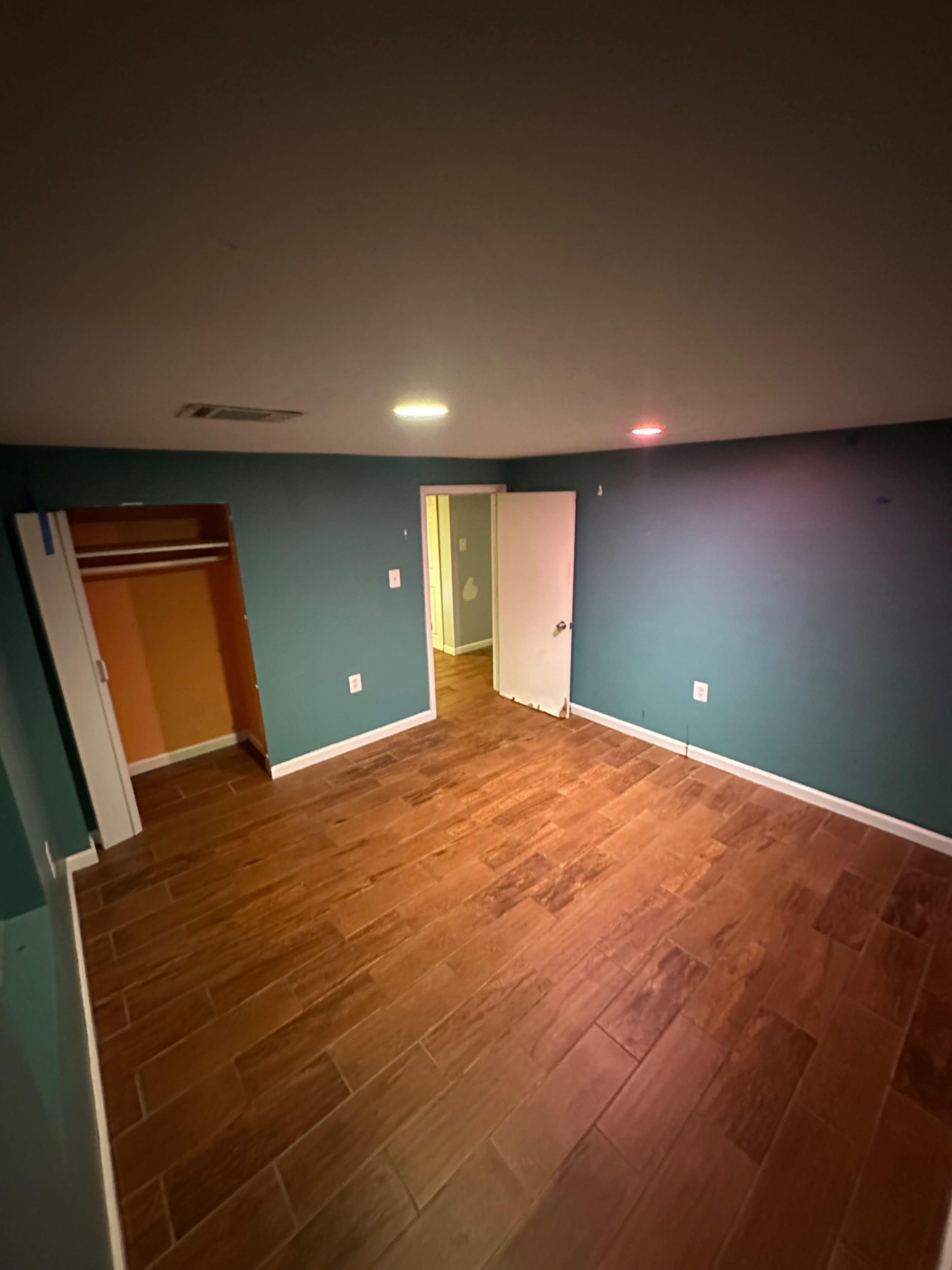 The image shows a dimly lit room with teal walls, a tiled floor, and an open closet on one side.