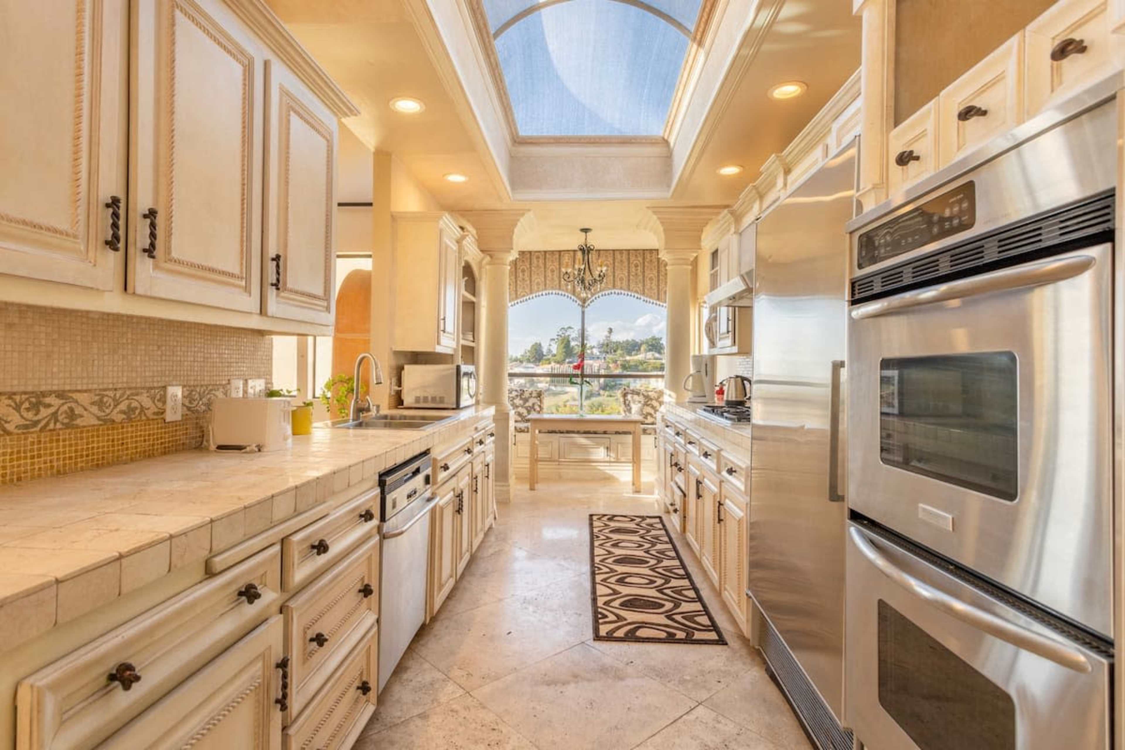 A spacious kitchen with cream-colored cabinets, stainless steel appliances, and a central island, illuminated by natural light from a skylight.