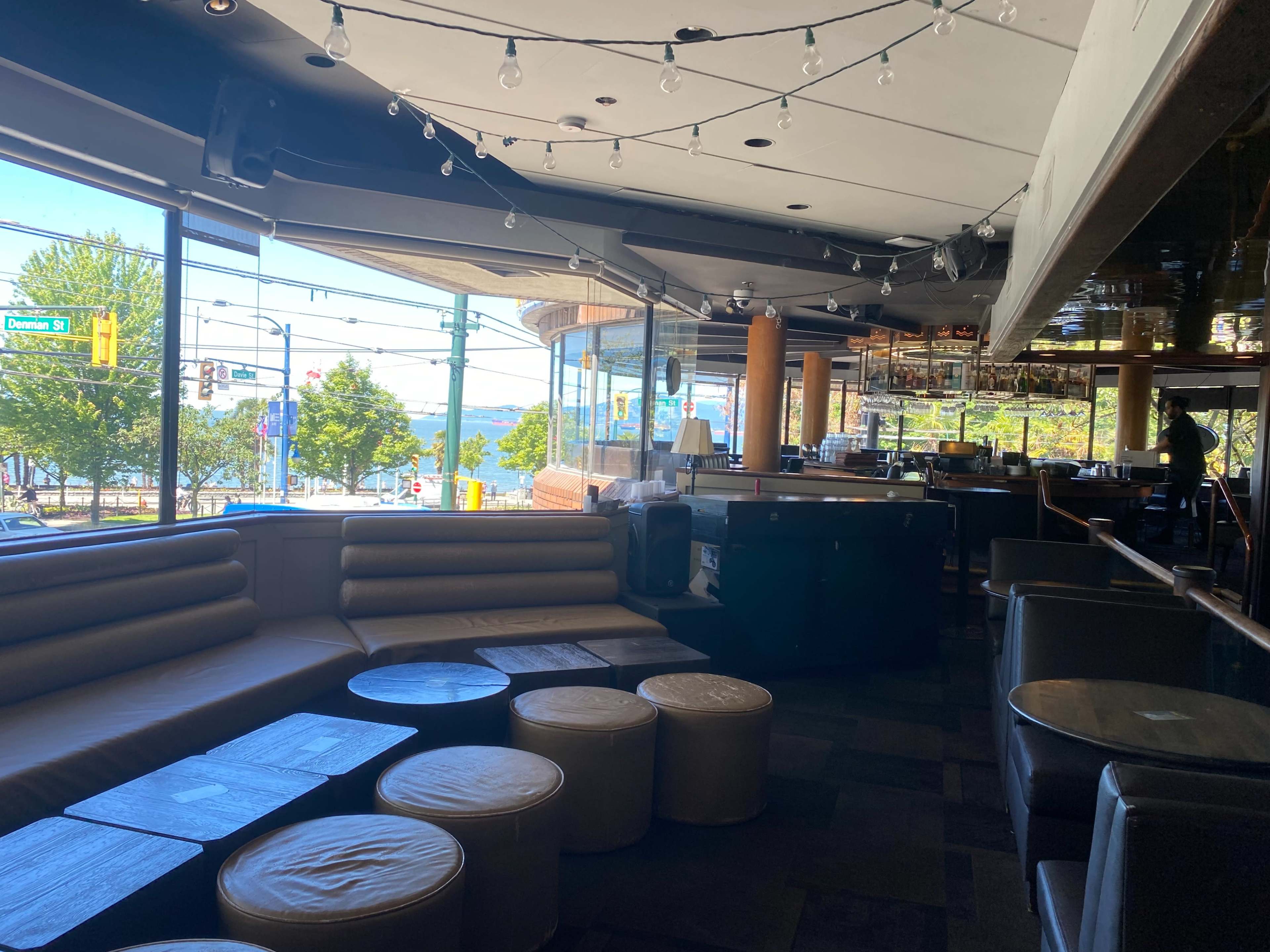 The interior of a restaurant or bar with a seating area, circular tables, and large windows overlooking a view outside.