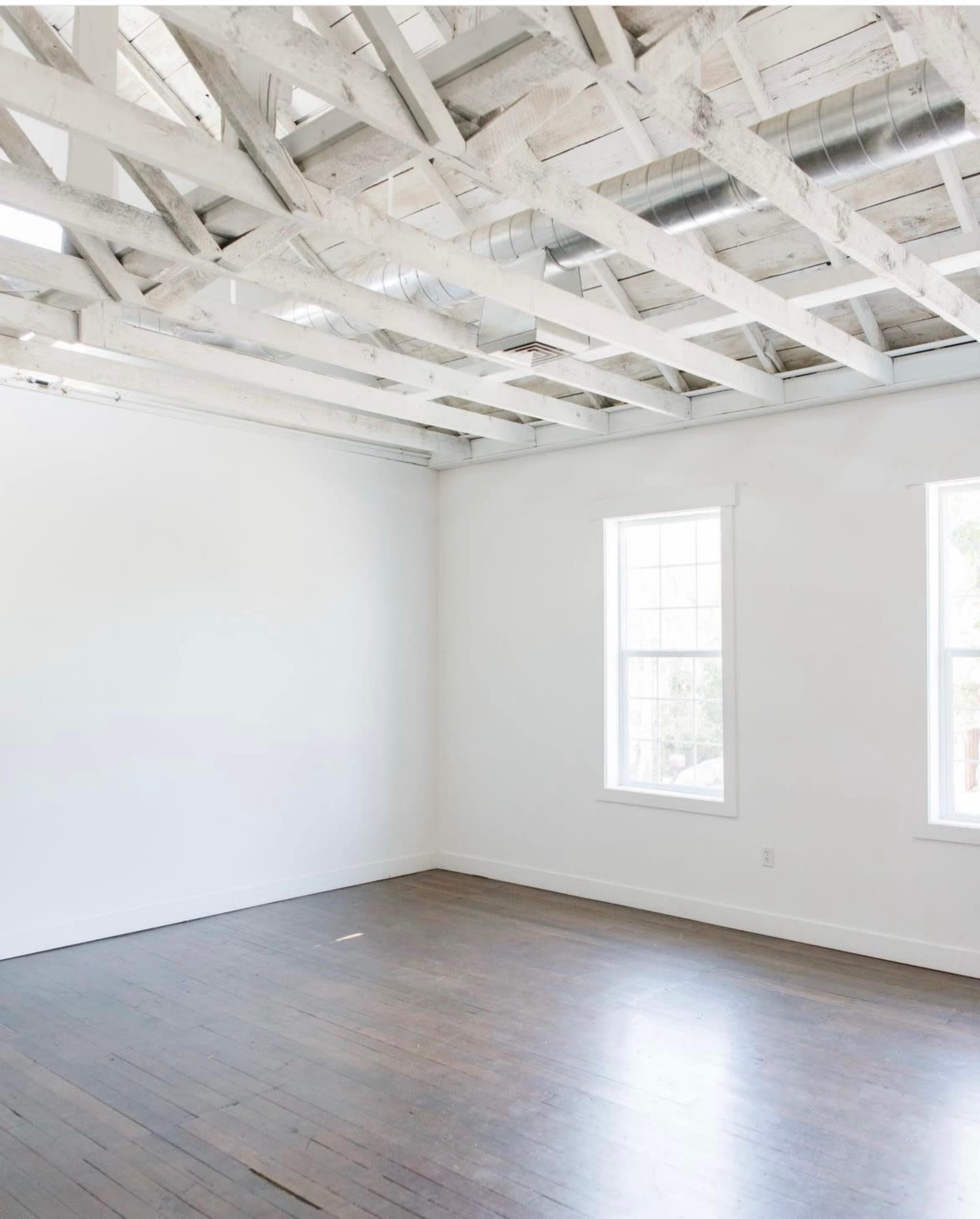 A minimally furnished room with white walls, a wooden floor, and exposed beams on the ceiling.
