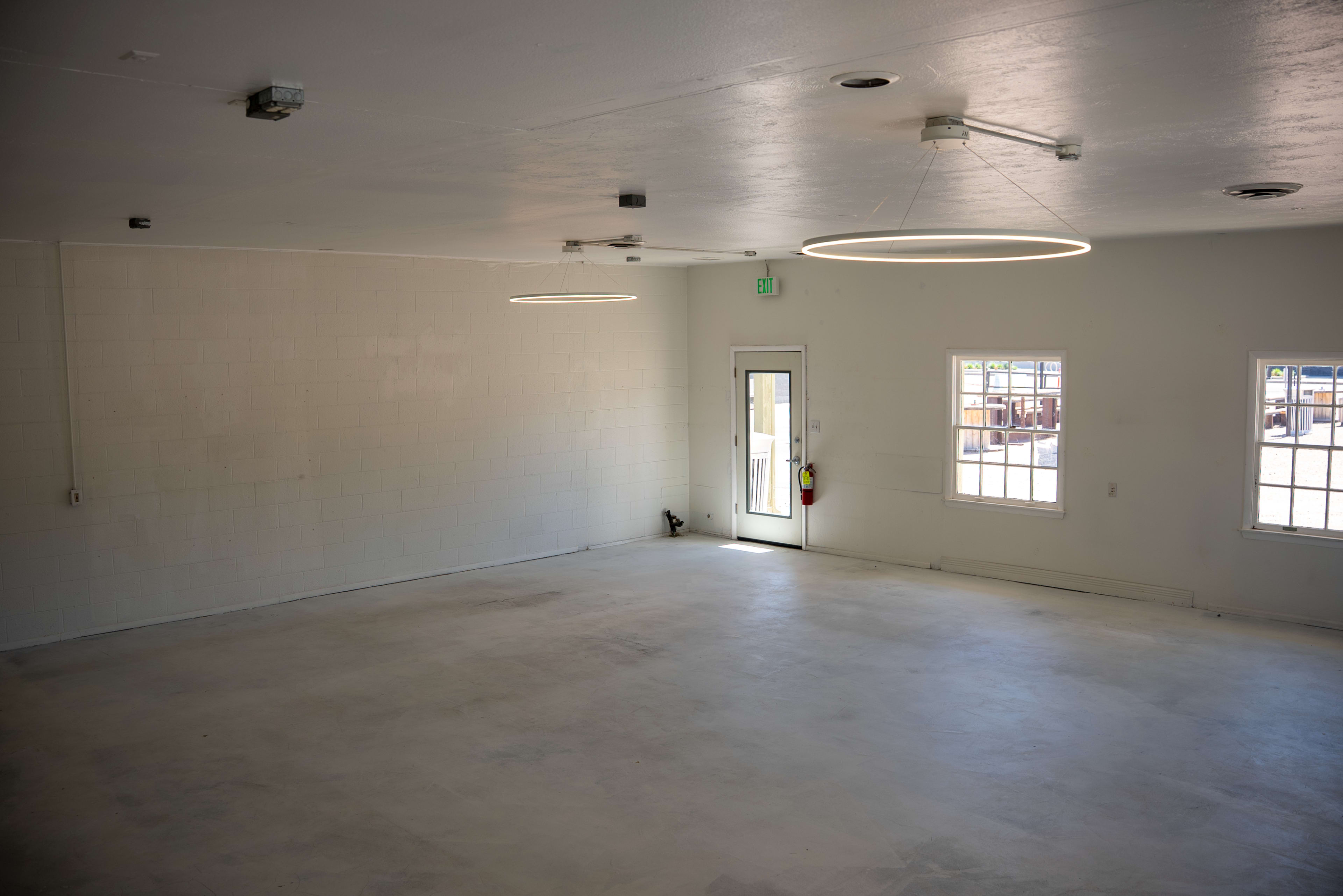 The image shows an empty room with white walls, circular ceiling lights, and a door leading outside.