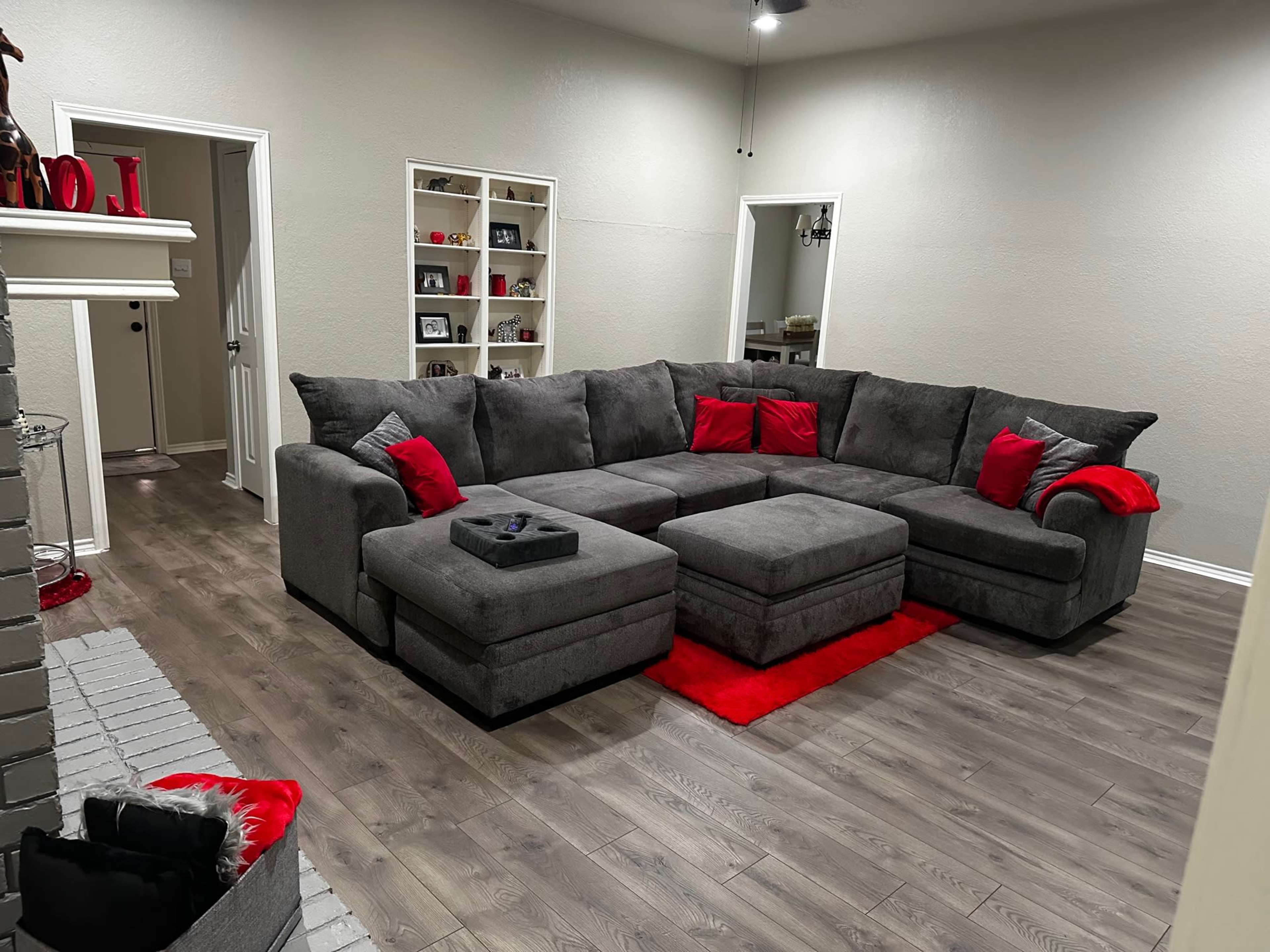 A gray sectional couch with red accent pillows situated in a modern living room featuring light-colored walls and wooden flooring.