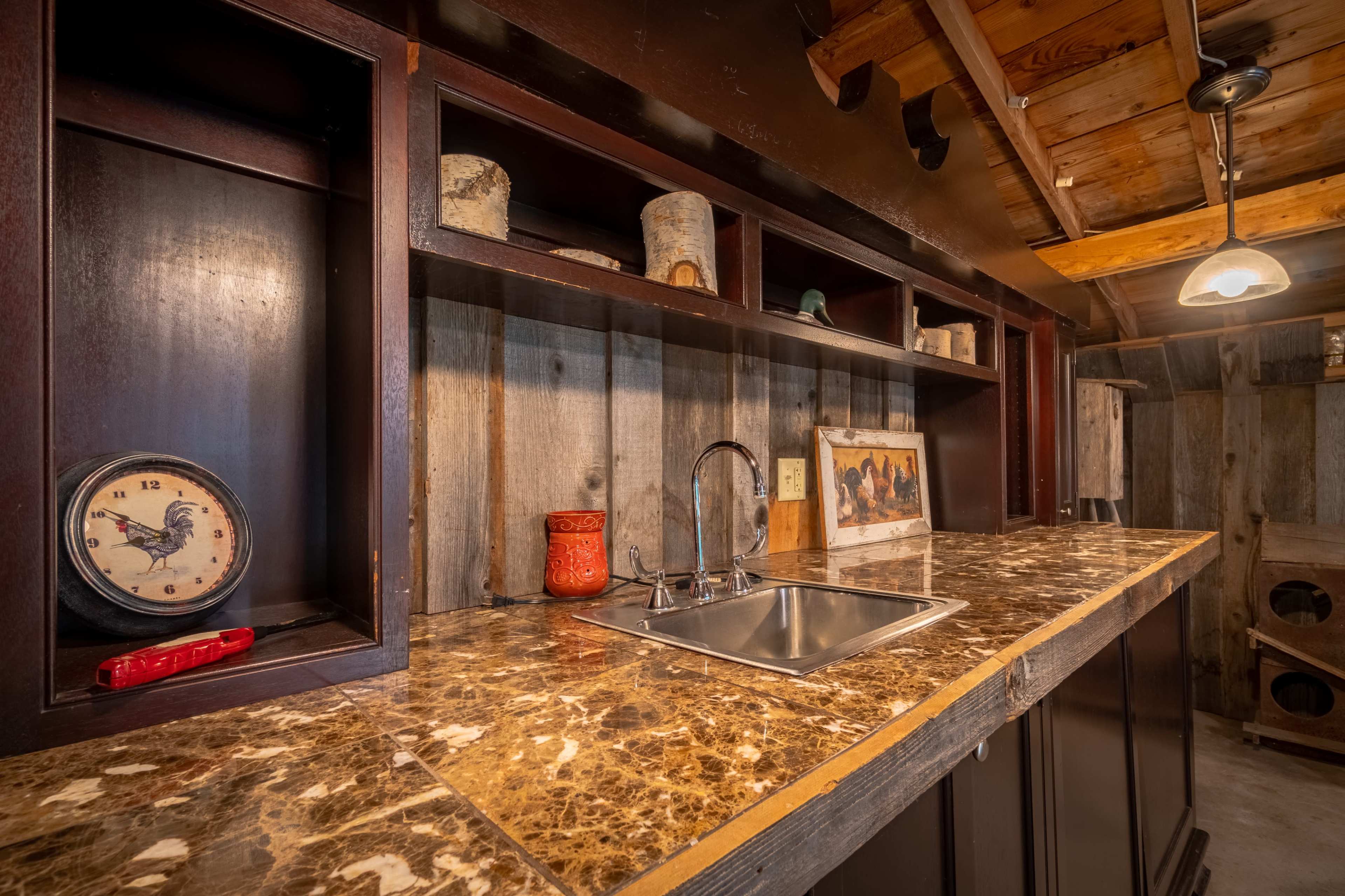 The image shows a rustic kitchen countertop with a sink, wood shelving, and various decorative items against a wooden wall.