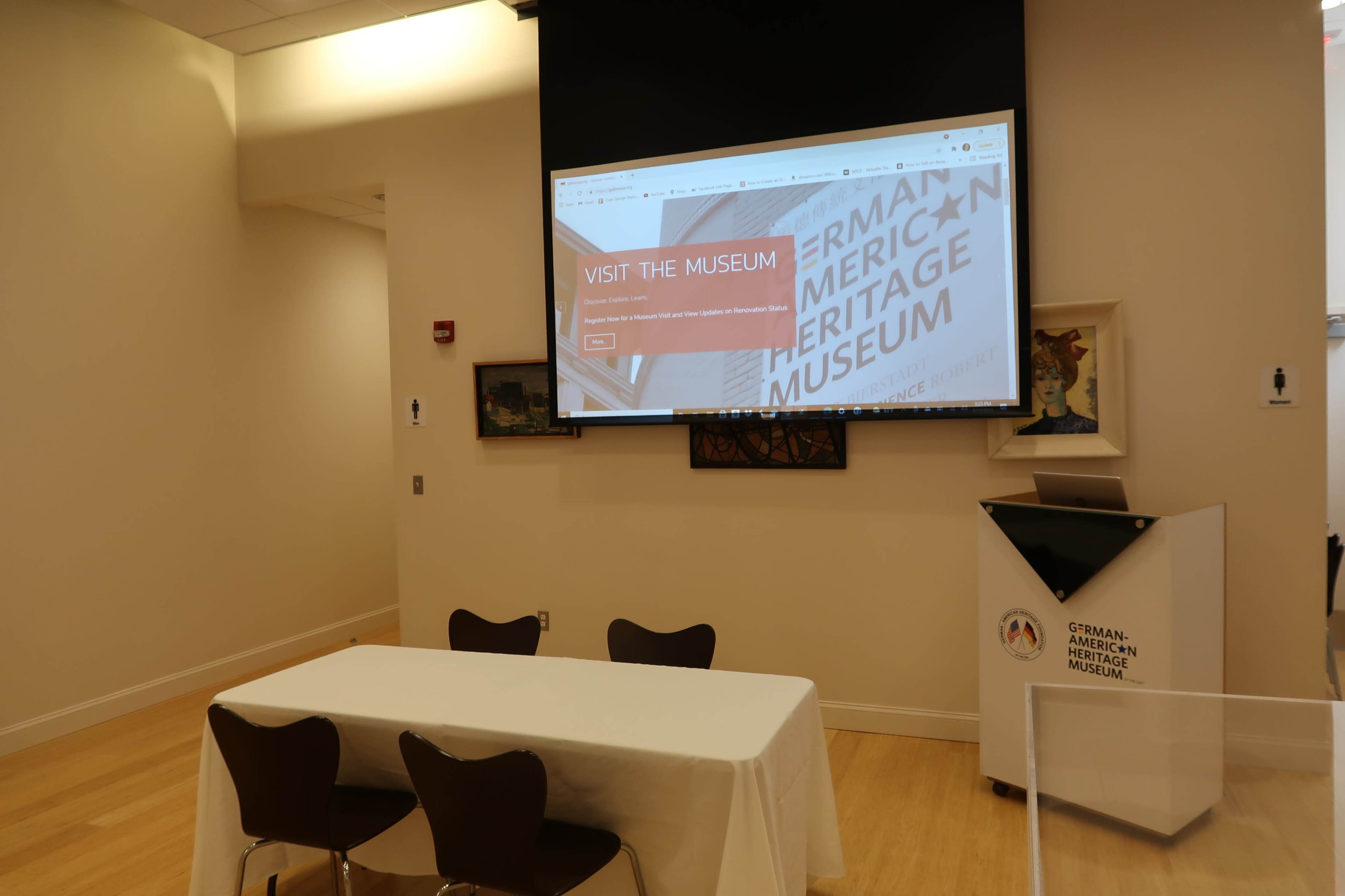A display screen with a website for the German-American Heritage Museum in a room featuring a table and chairs.