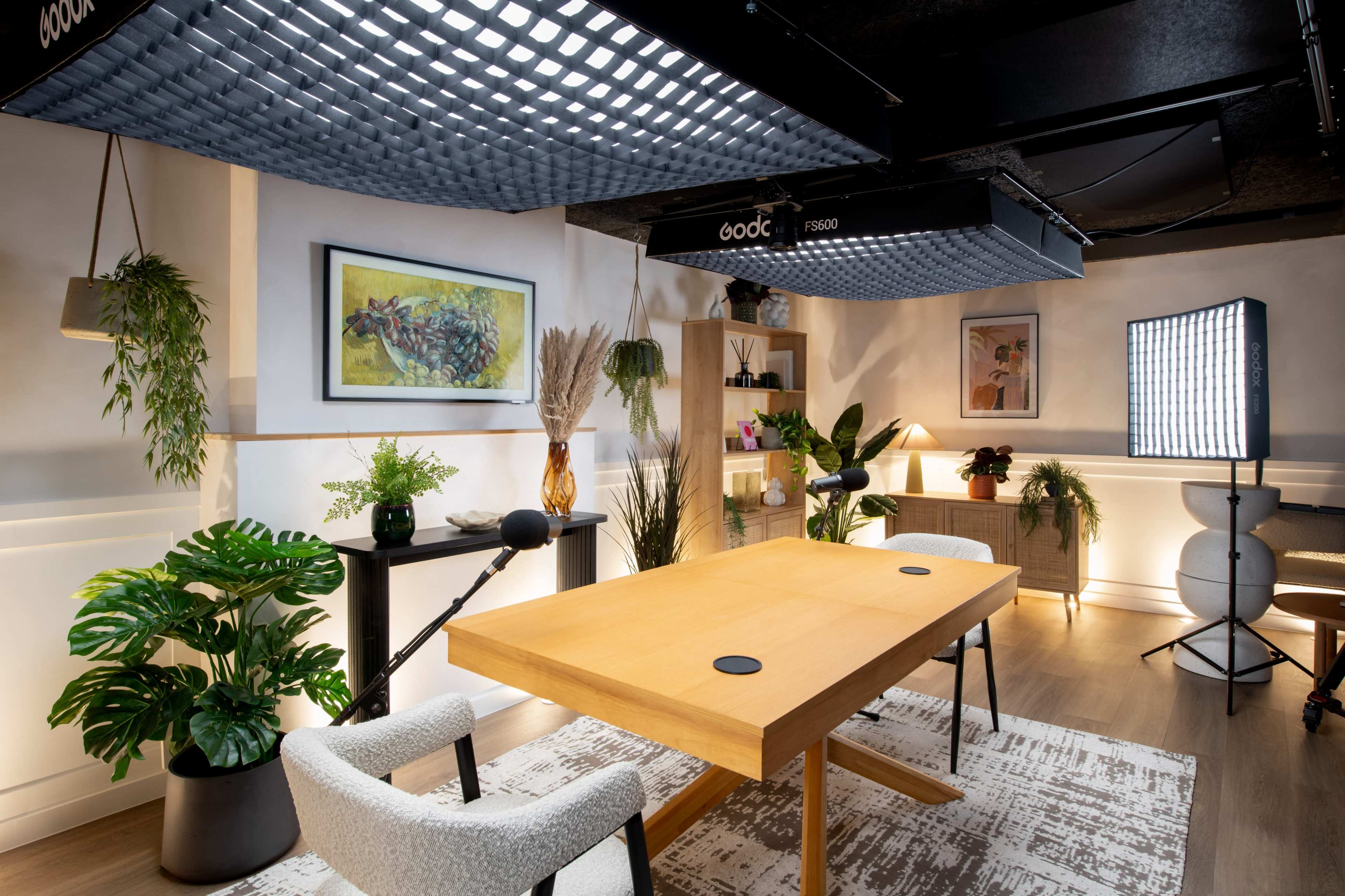 A modern conference room features a wooden table, two chairs, plants, and a backdrop with artwork, illuminated by soft lighting.